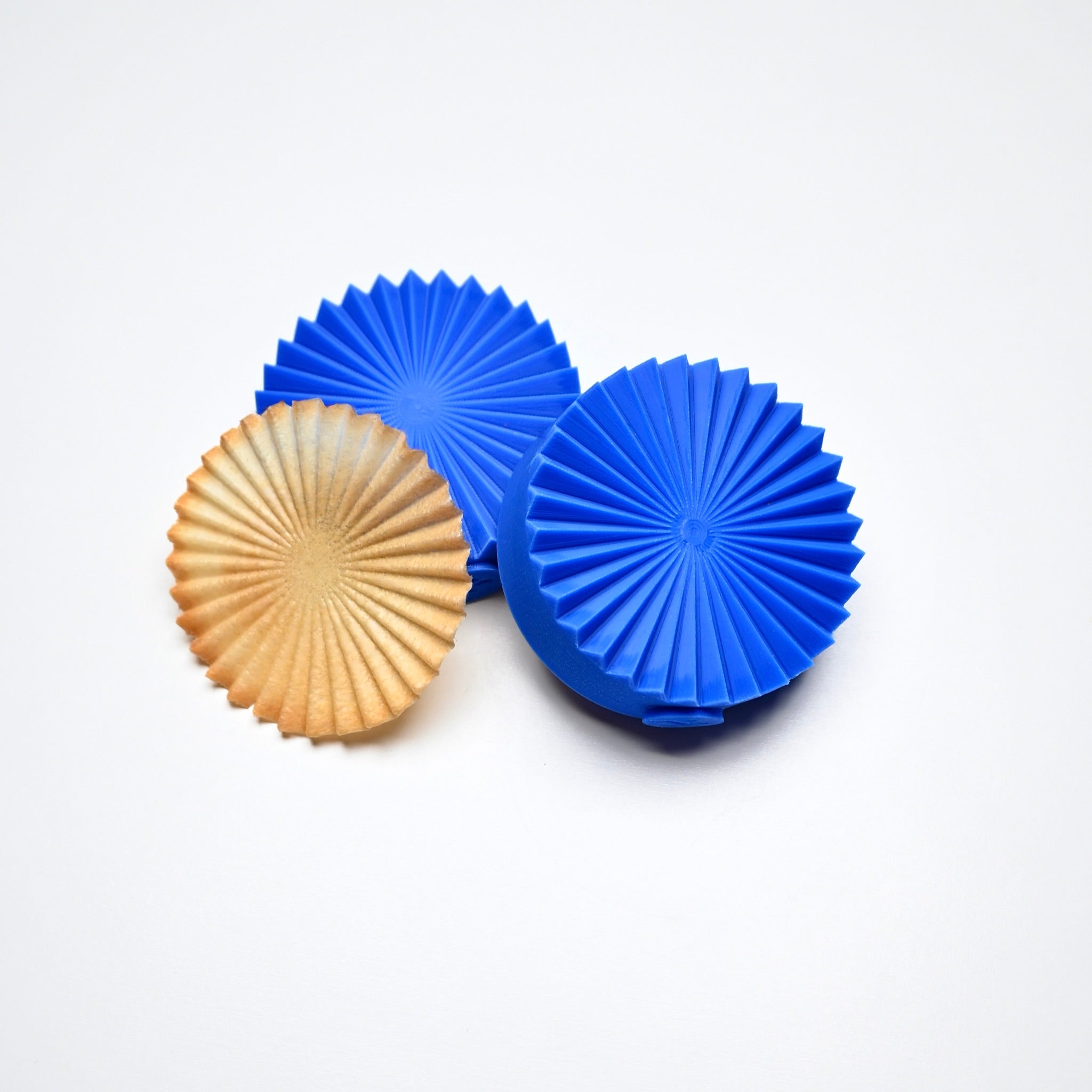 Blue silicone fan pastry molds next to a matching ribbed golden tuile cookie.