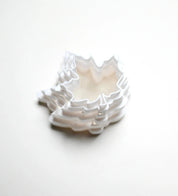 Stack of white plastic maple leaf cookie cutters in various sizes on a white background.