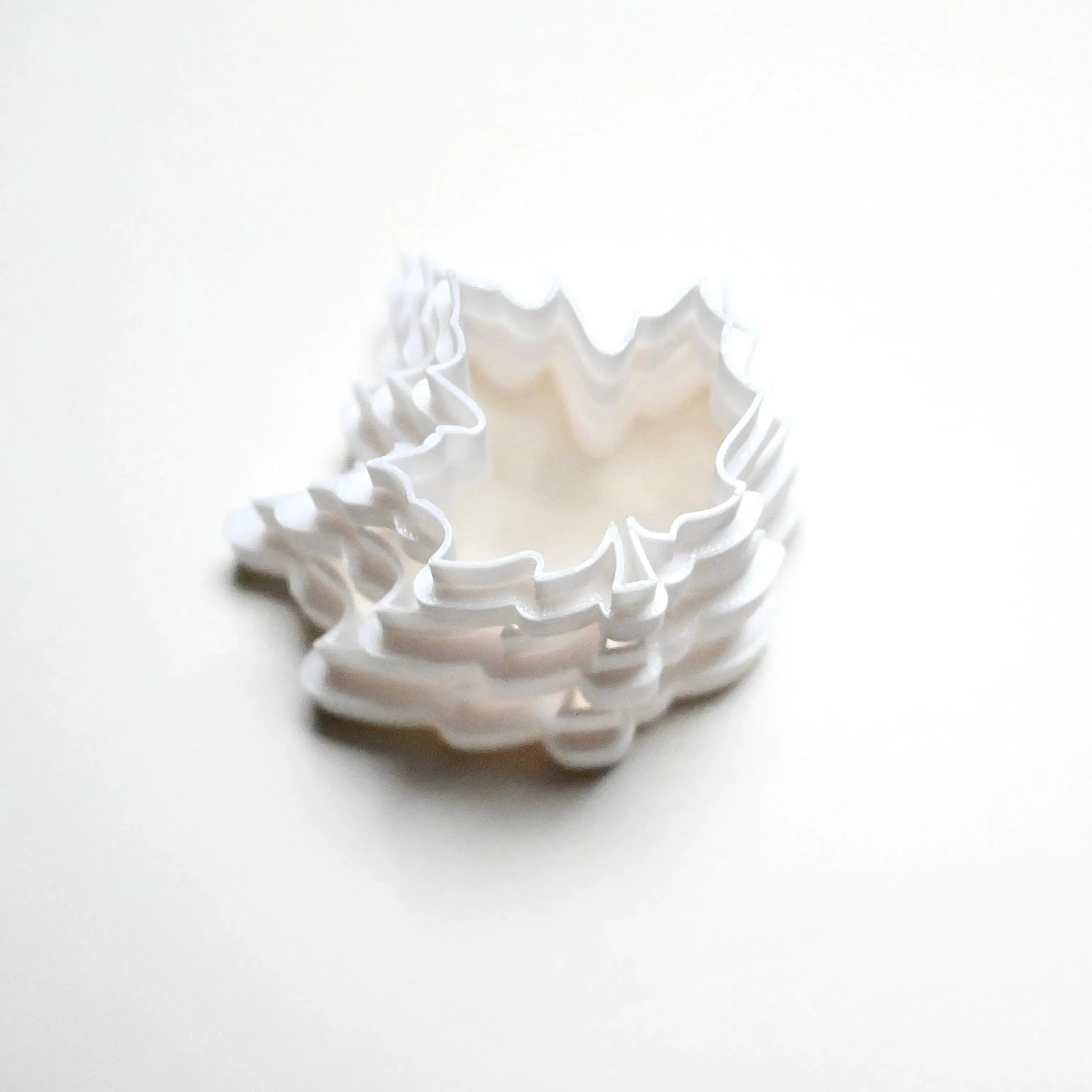 Stack of white plastic maple leaf cookie cutters in various sizes on a white background.