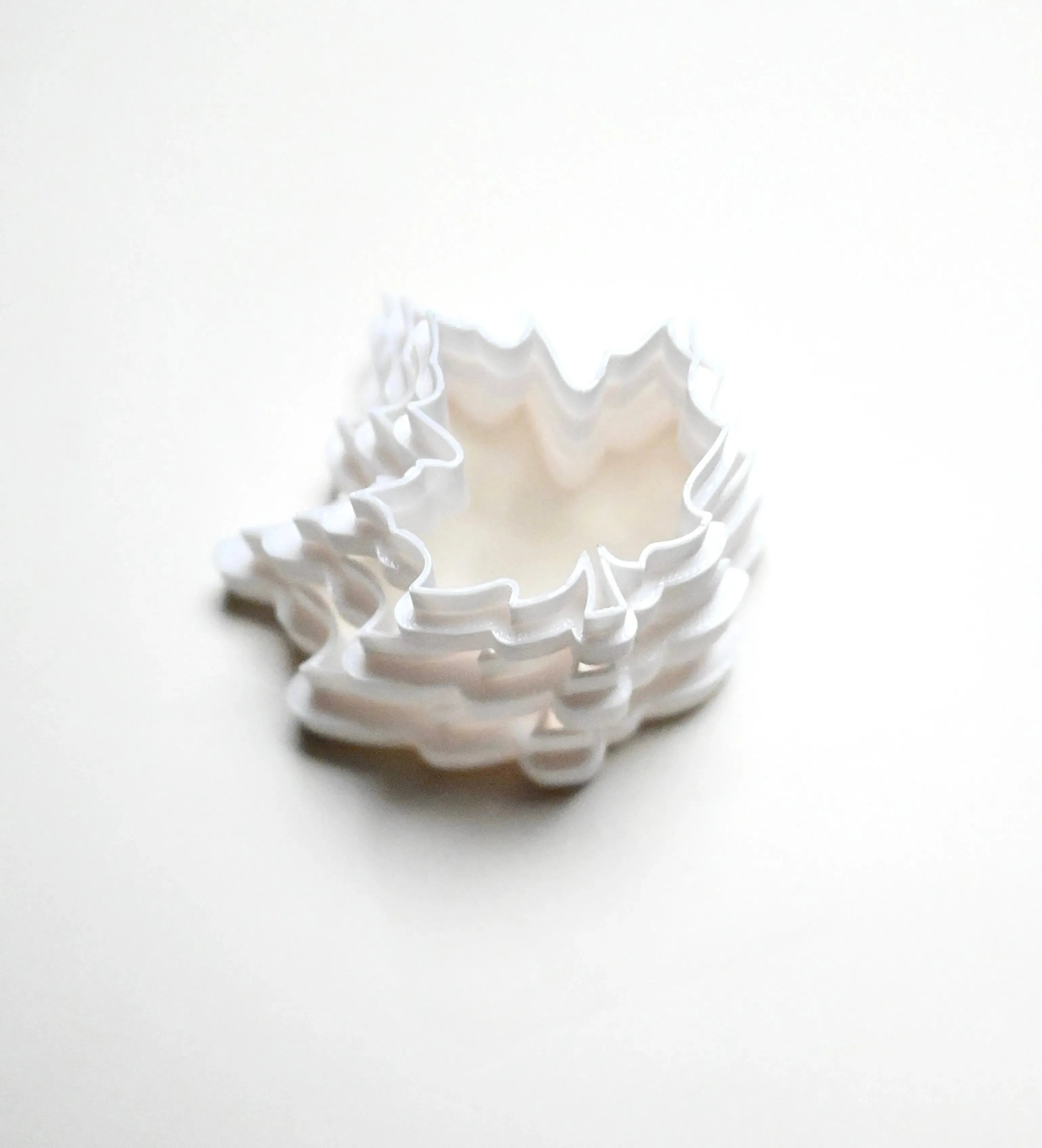 Stack of white plastic maple leaf cookie cutters in various sizes on a white background.