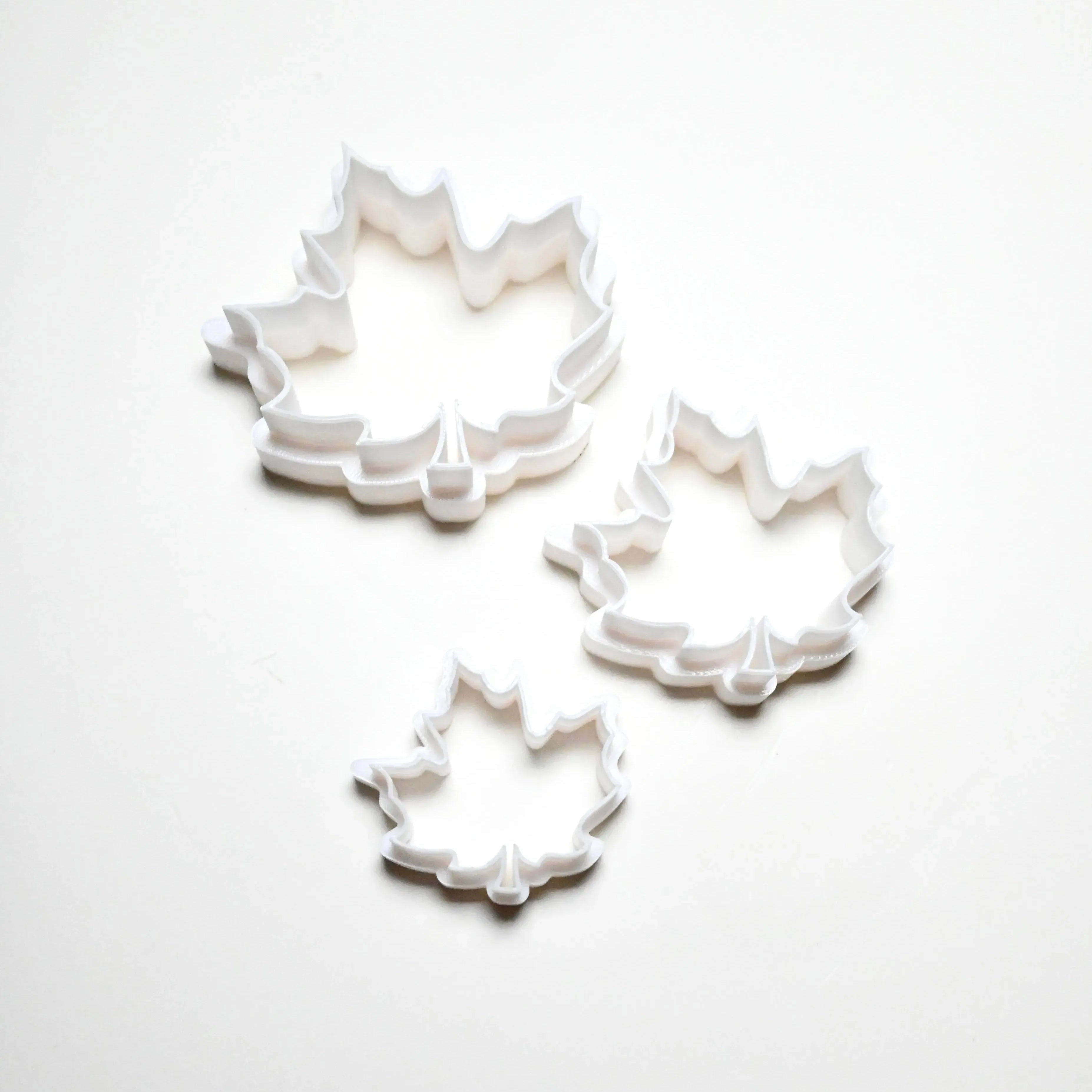 Three white plastic maple leaf cookie cutters in small, medium, and large sizes.