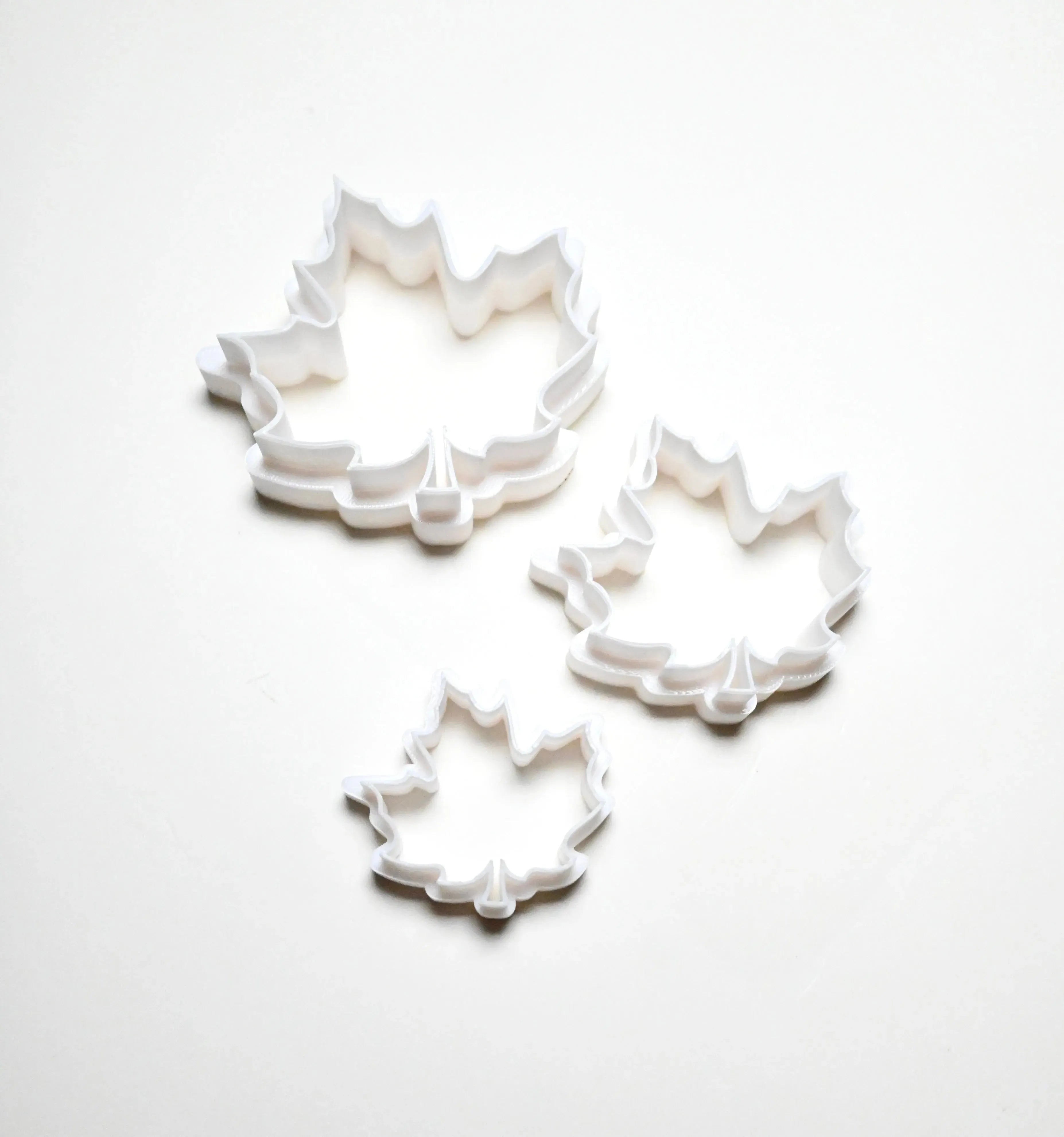Three white plastic maple leaf cookie cutters in small, medium, and large sizes.