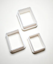 Three white plastic fluted rectangle cookie cutters in different sizes.