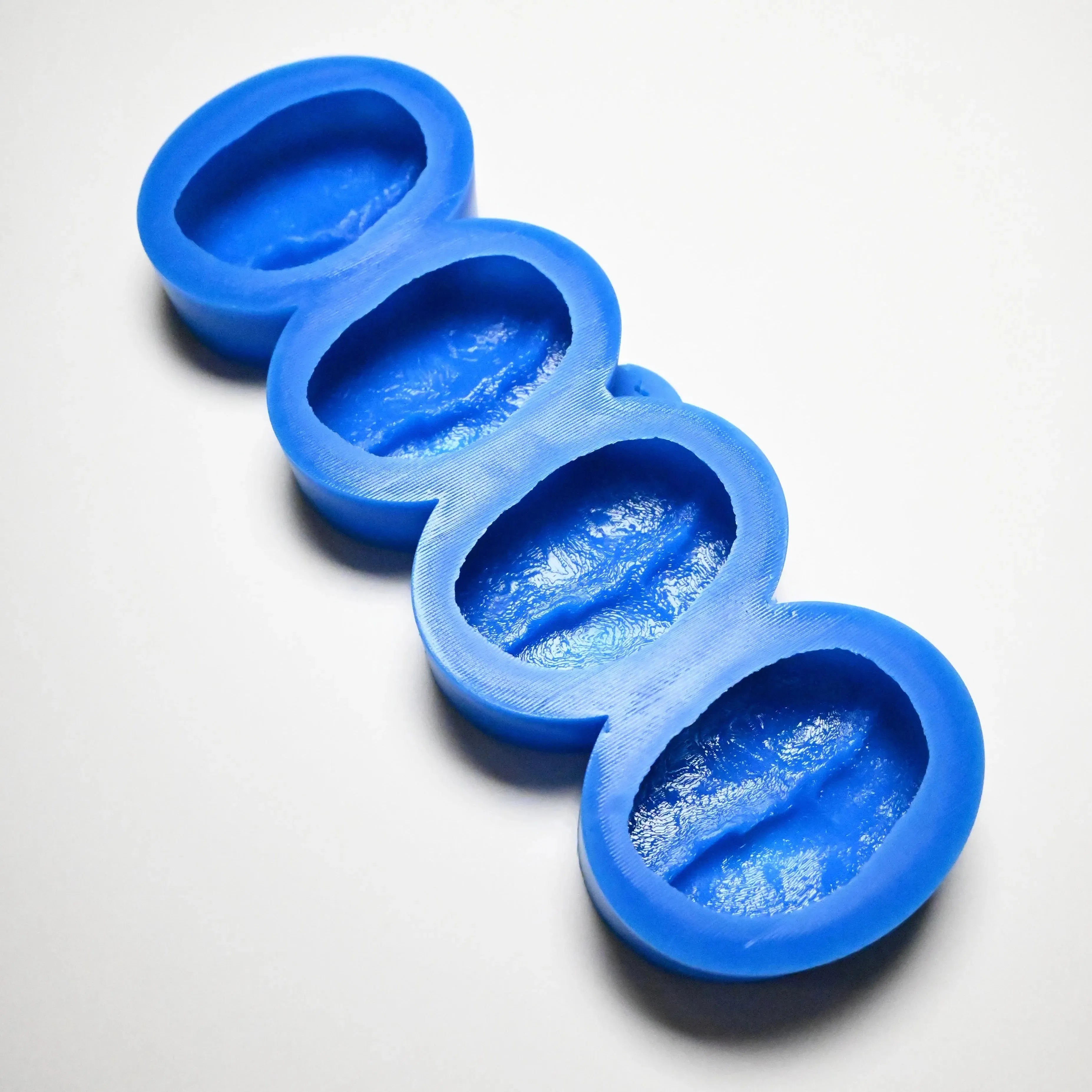 Blue silicone mold with four detailed coffee bean shaped cavities.