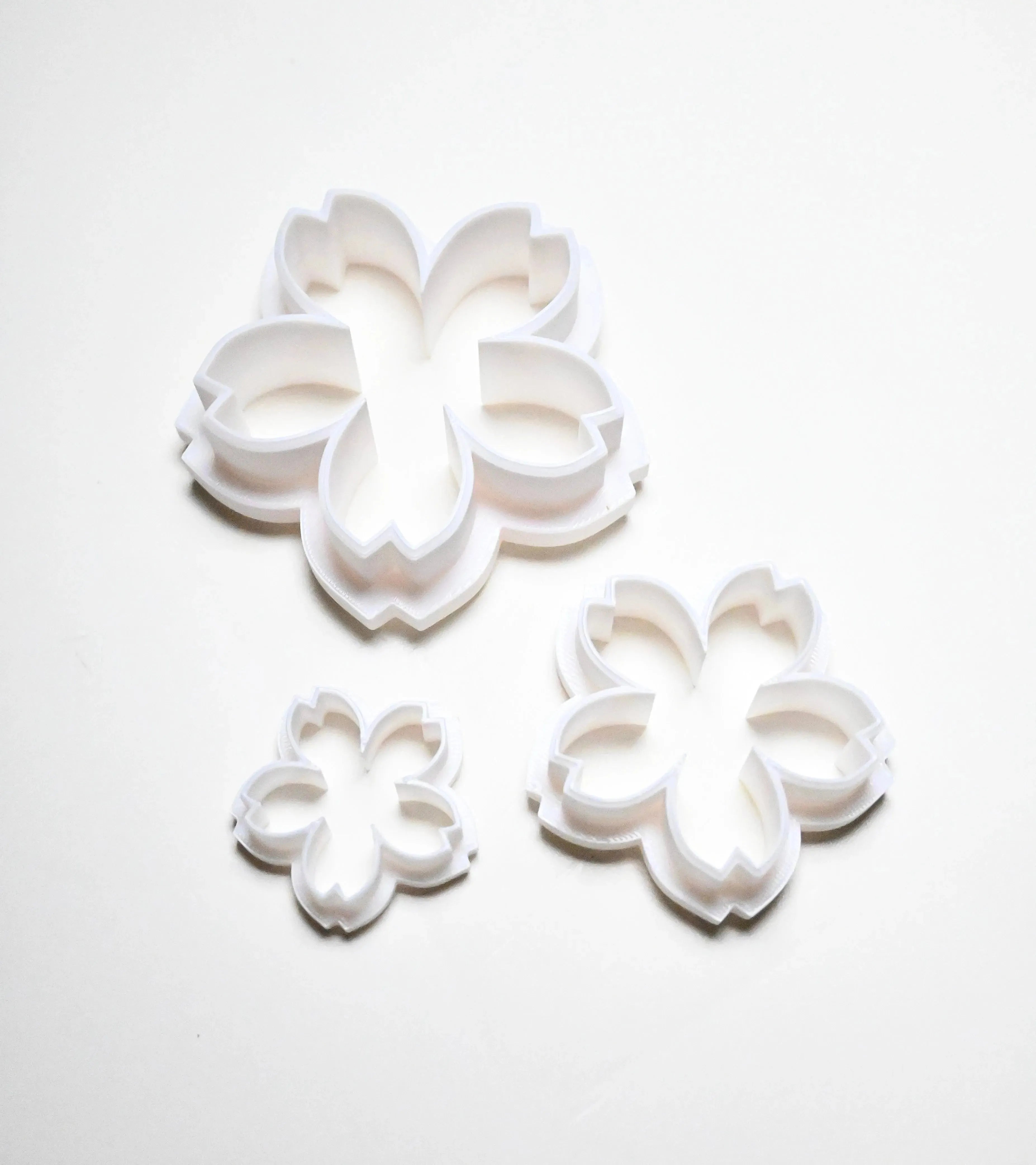 Three white plastic sakura cherry blossom cookie cutters in small, medium, and large sizes.