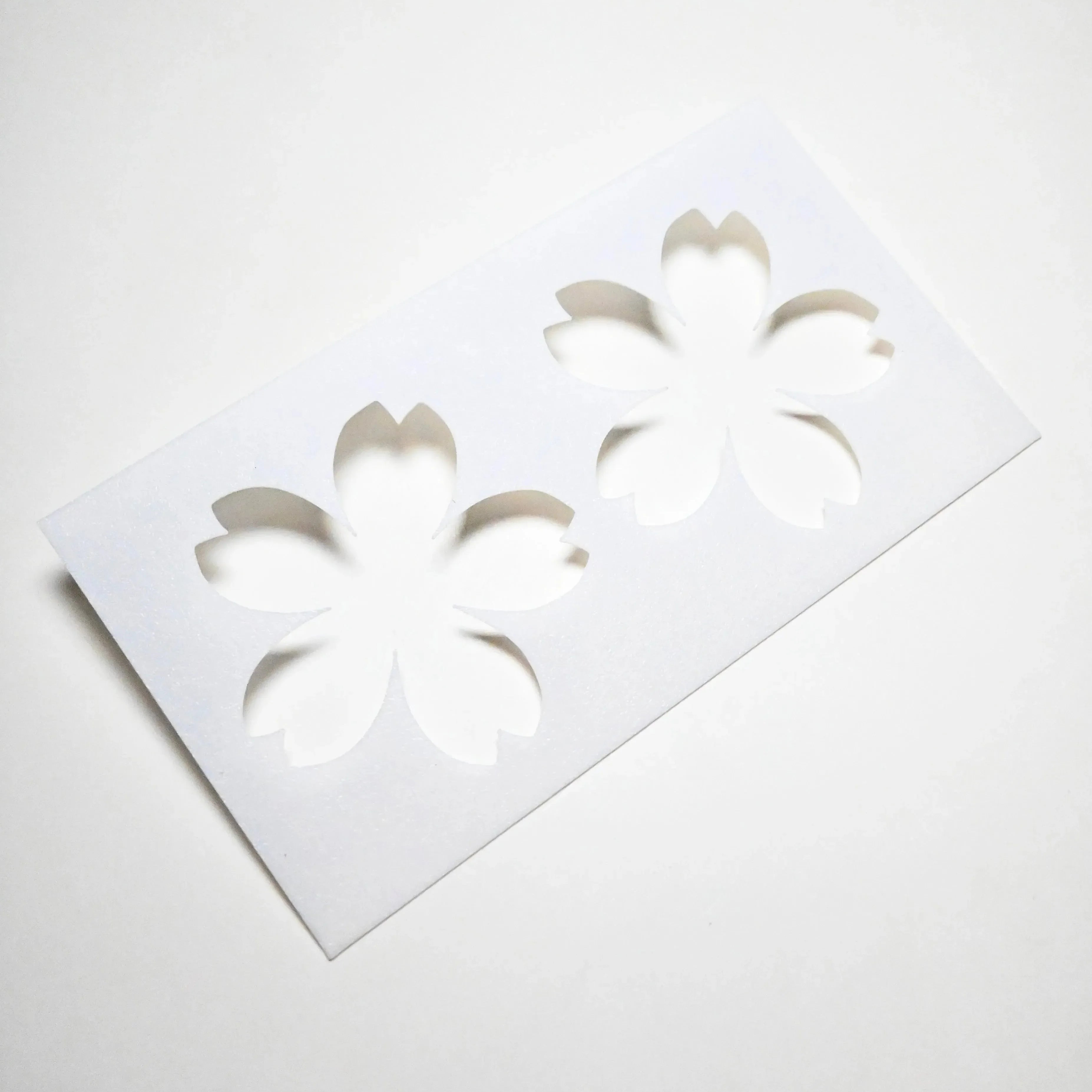 White plastic Sakura pastry stencil with two cherry blossom flower cutouts.