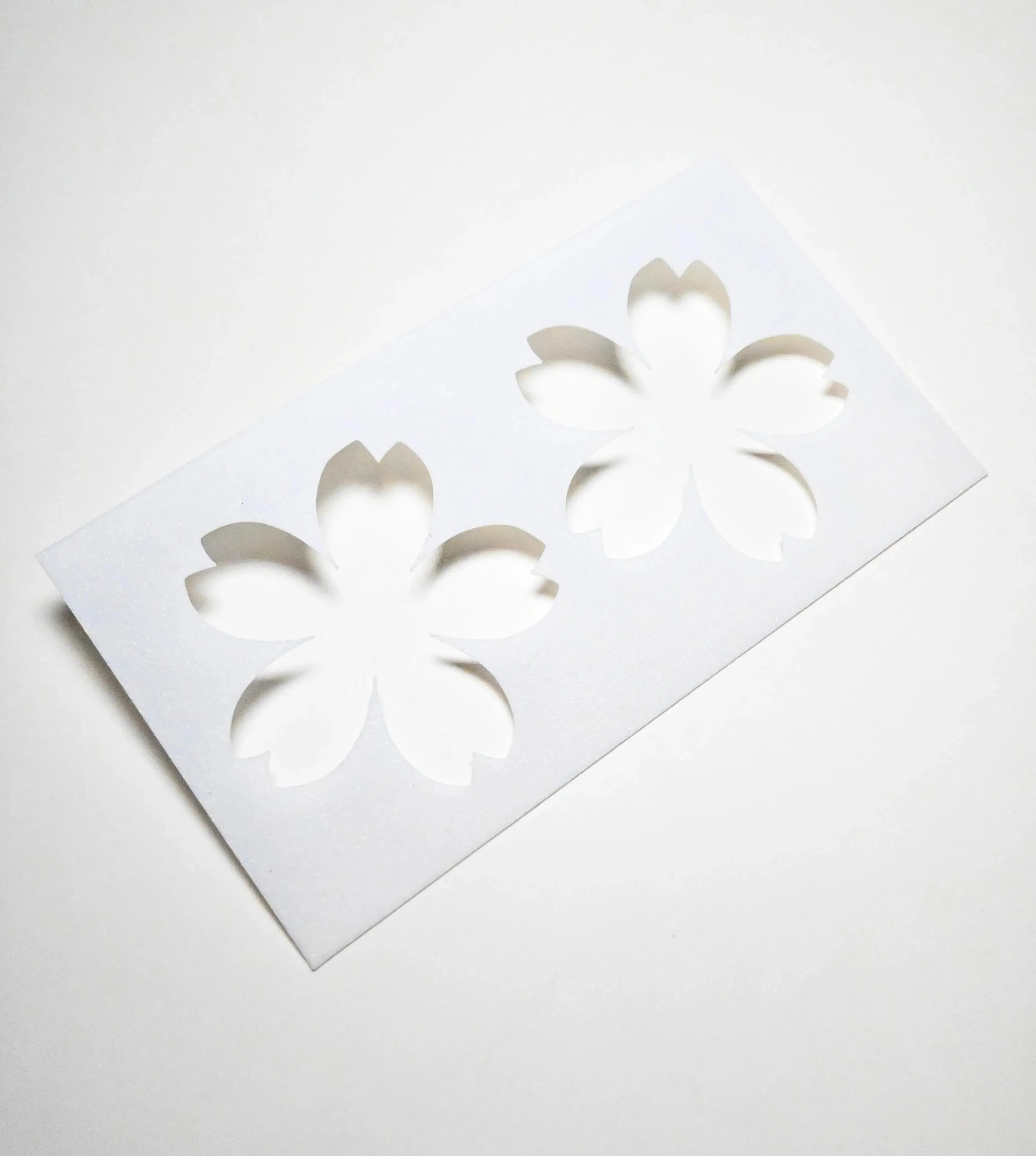 White plastic Sakura pastry stencil with two cherry blossom flower cutouts.
