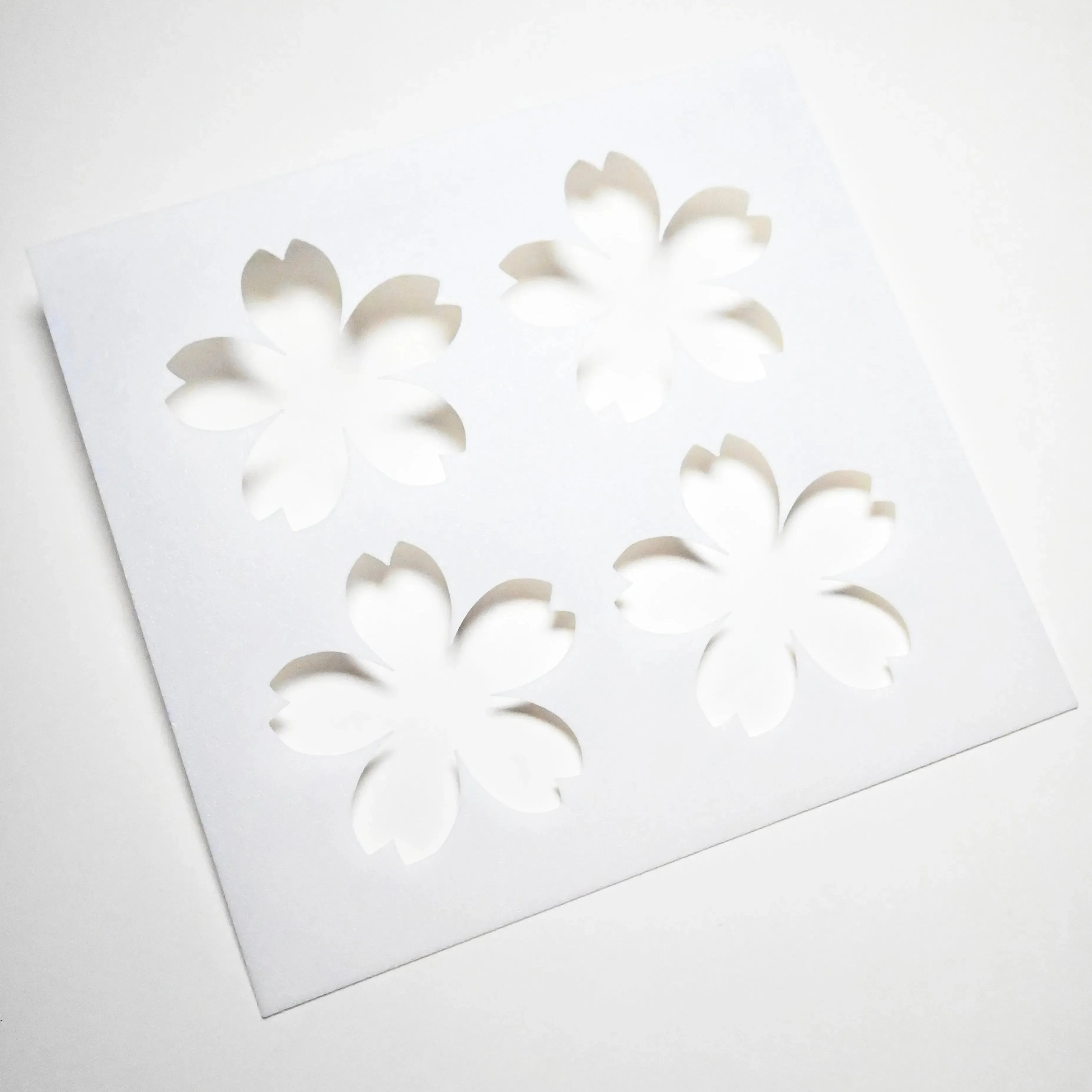 White square pastry stencil with four cherry blossom sakura cutouts.