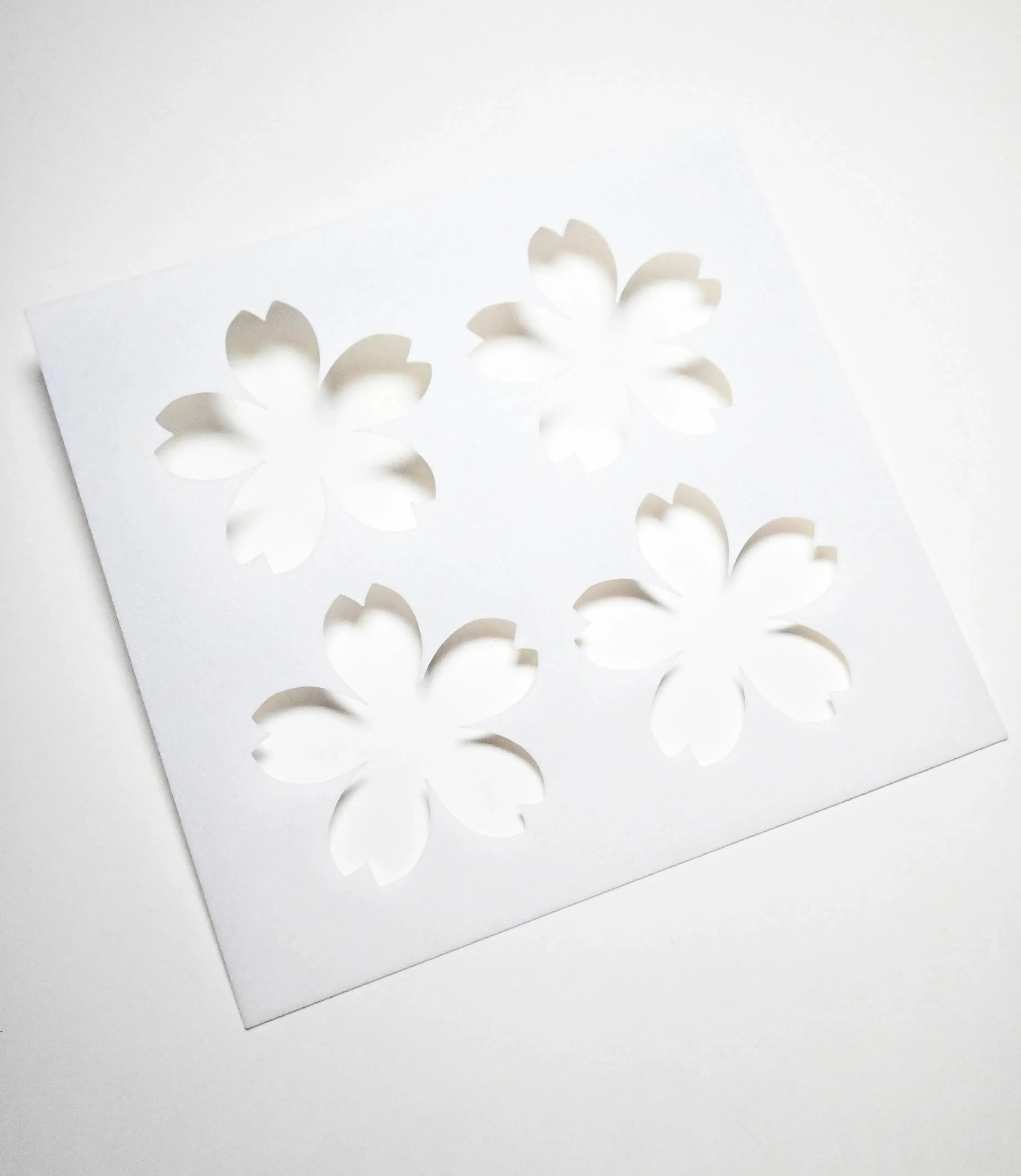 White square pastry stencil with four cherry blossom sakura cutouts.