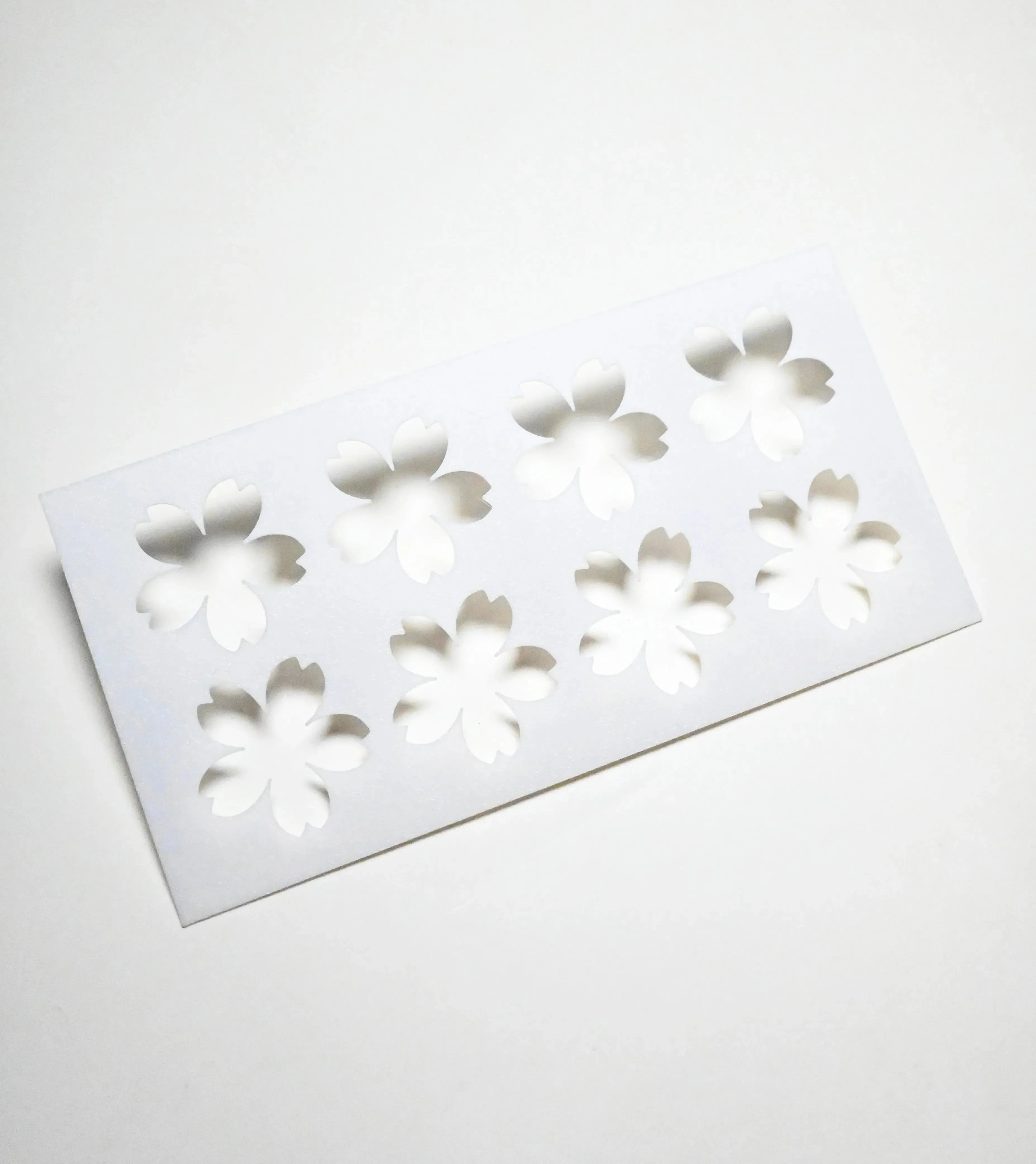 White plastic Sakura pastry stencil with eight cherry blossom shaped cutouts.