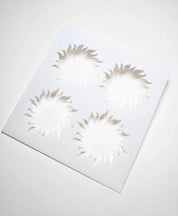 White square pastry stencil featuring four cutout sun shapes with wavy rays.