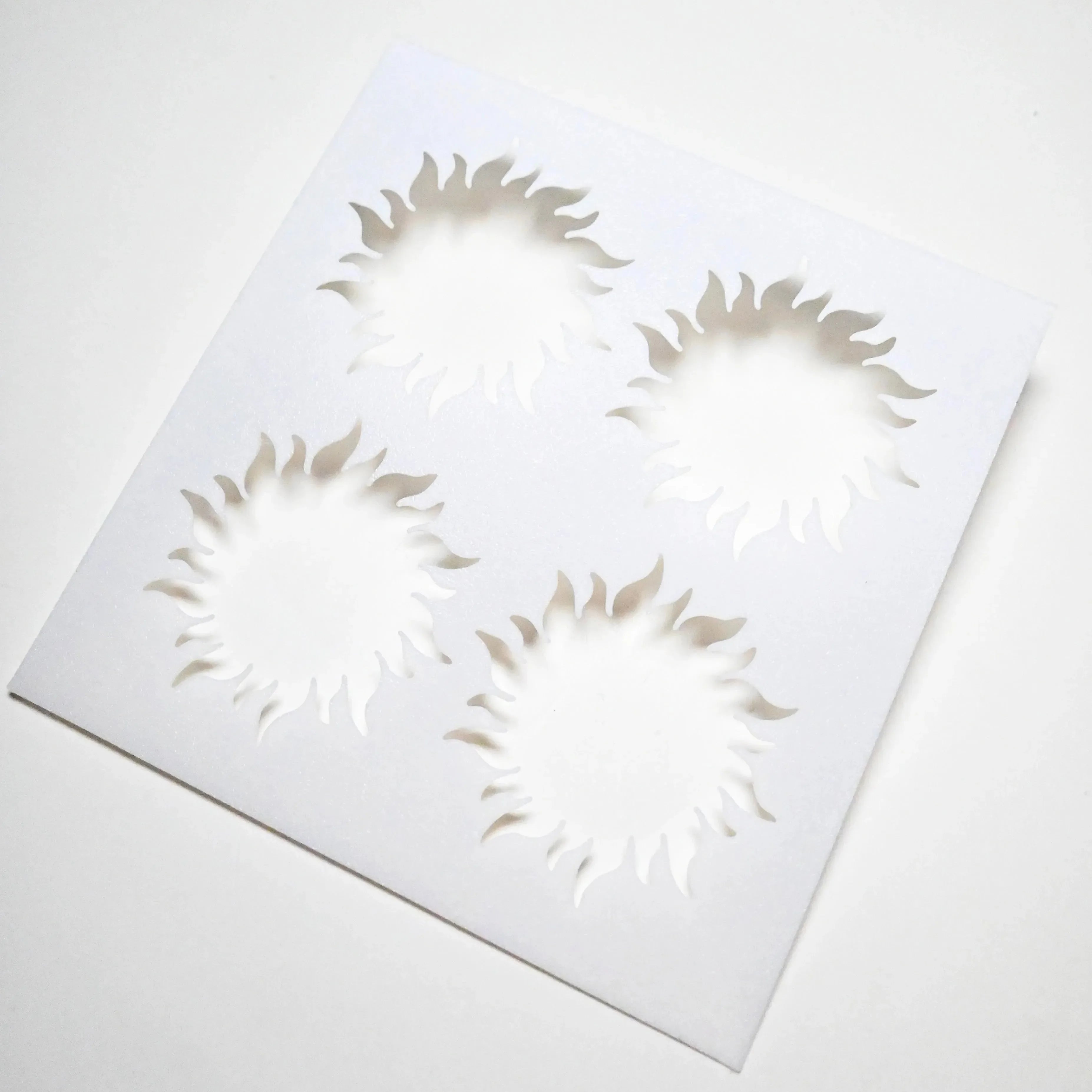 White square pastry stencil featuring four cutout sun shapes with wavy rays.