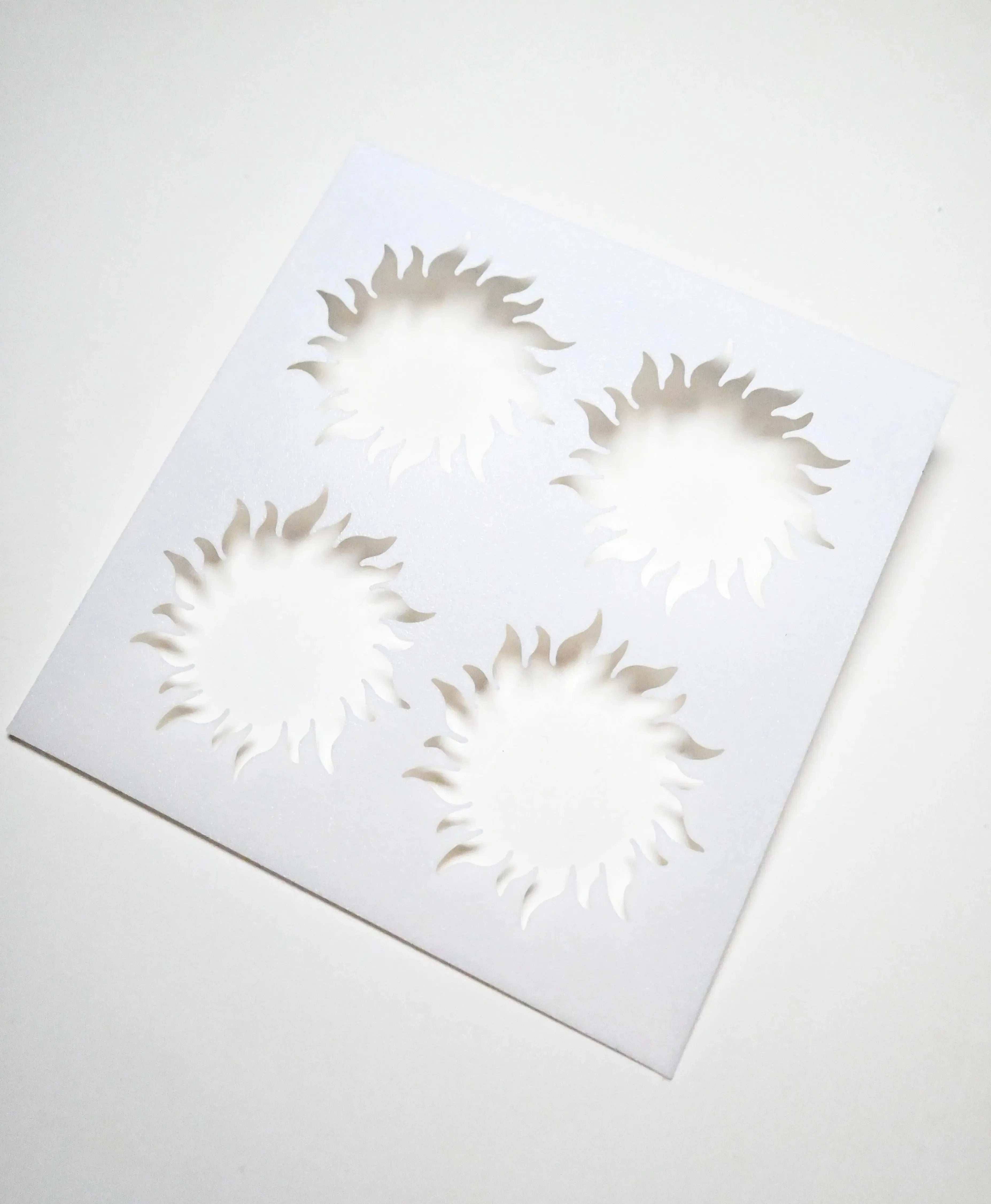 White square pastry stencil featuring four cutout sun shapes with wavy rays.