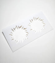 White plastic pastry stencil featuring two detailed sun-shaped cutouts with wavy rays.