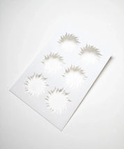 White plastic pastry stencil featuring six sun-shaped cutouts with wavy rays.