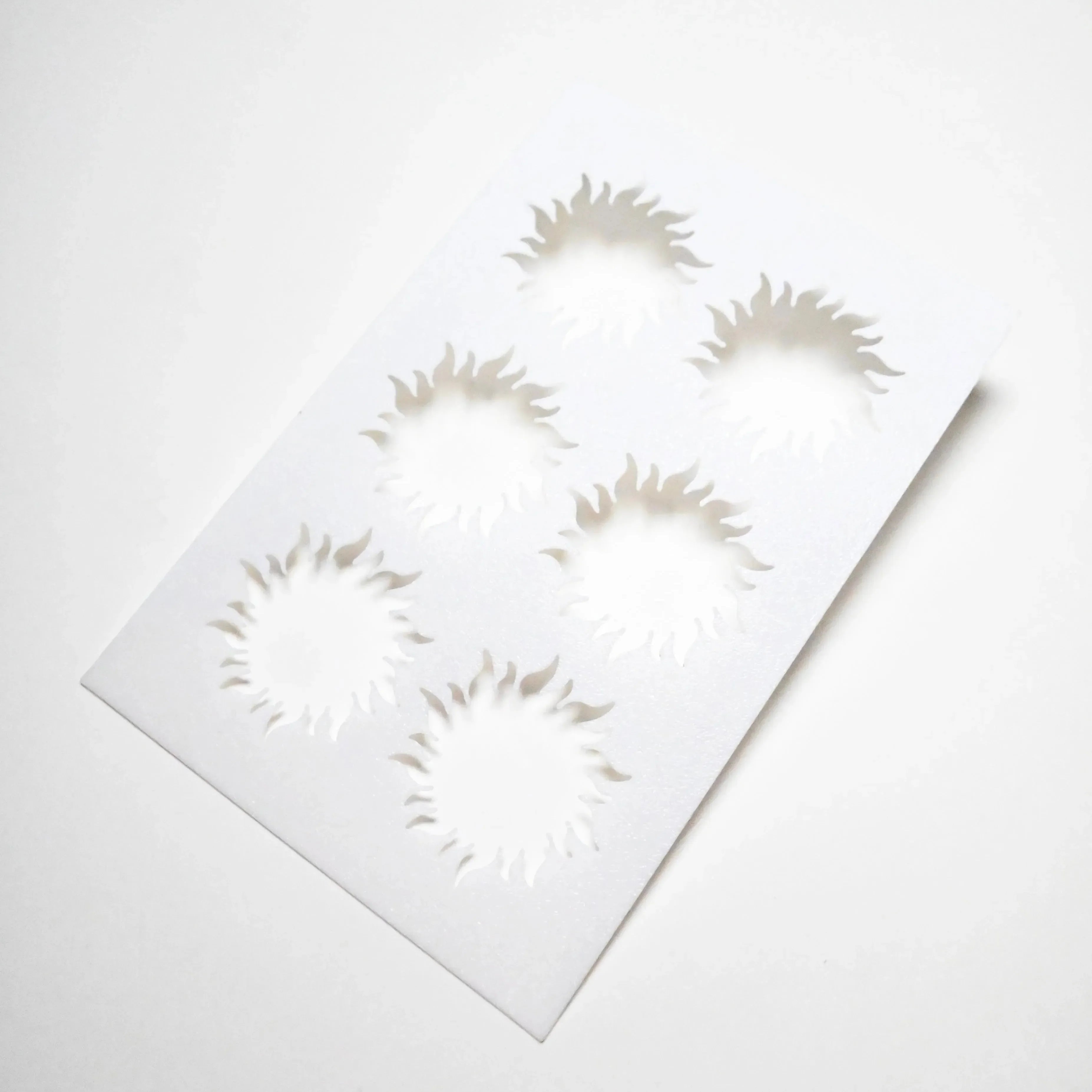 White plastic pastry stencil featuring six sun-shaped cutouts with wavy rays.