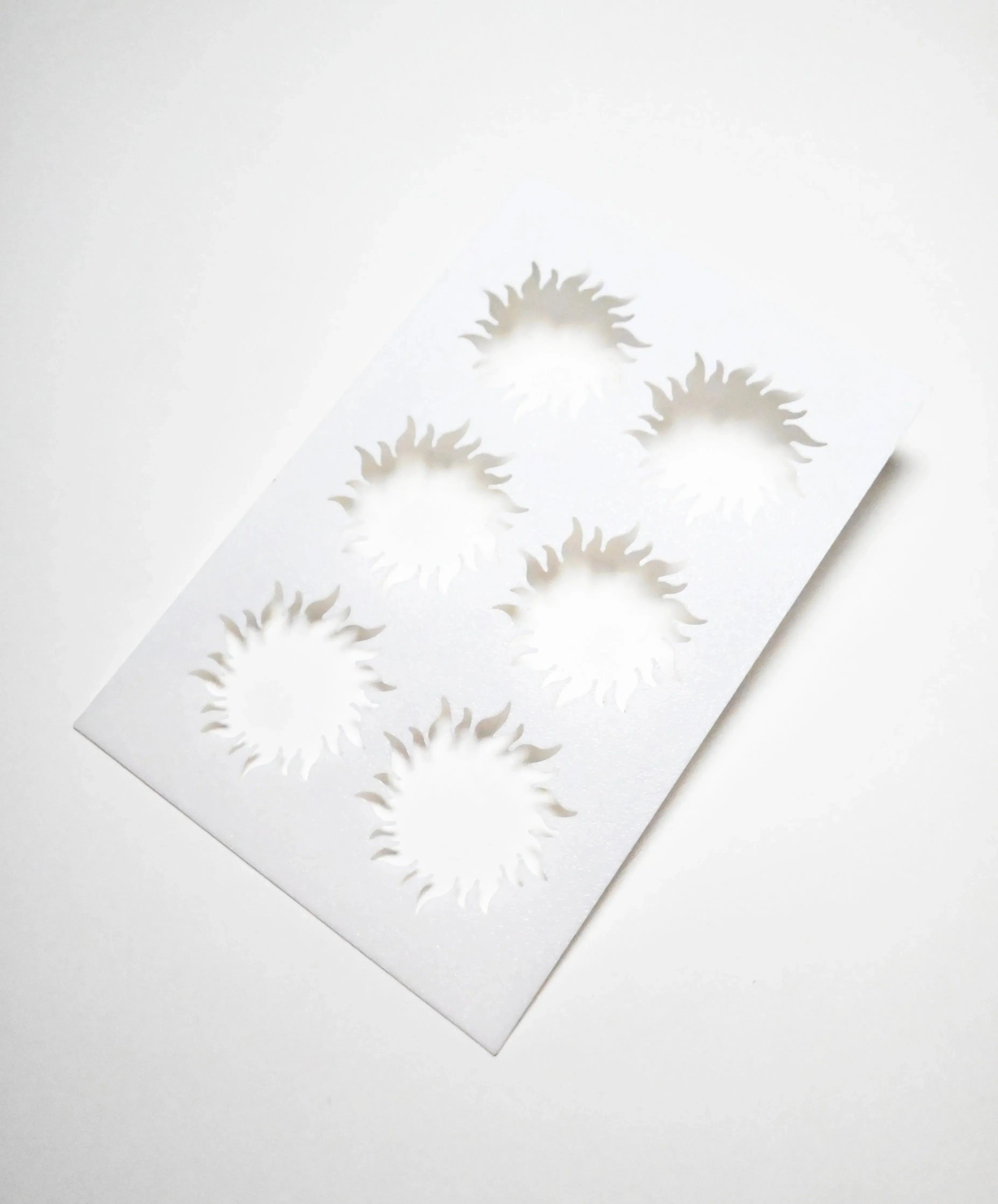 White plastic pastry stencil featuring six sun-shaped cutouts with wavy rays.