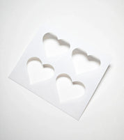 White plastic pastry stencil with four symmetrical heart-shaped cutouts.
