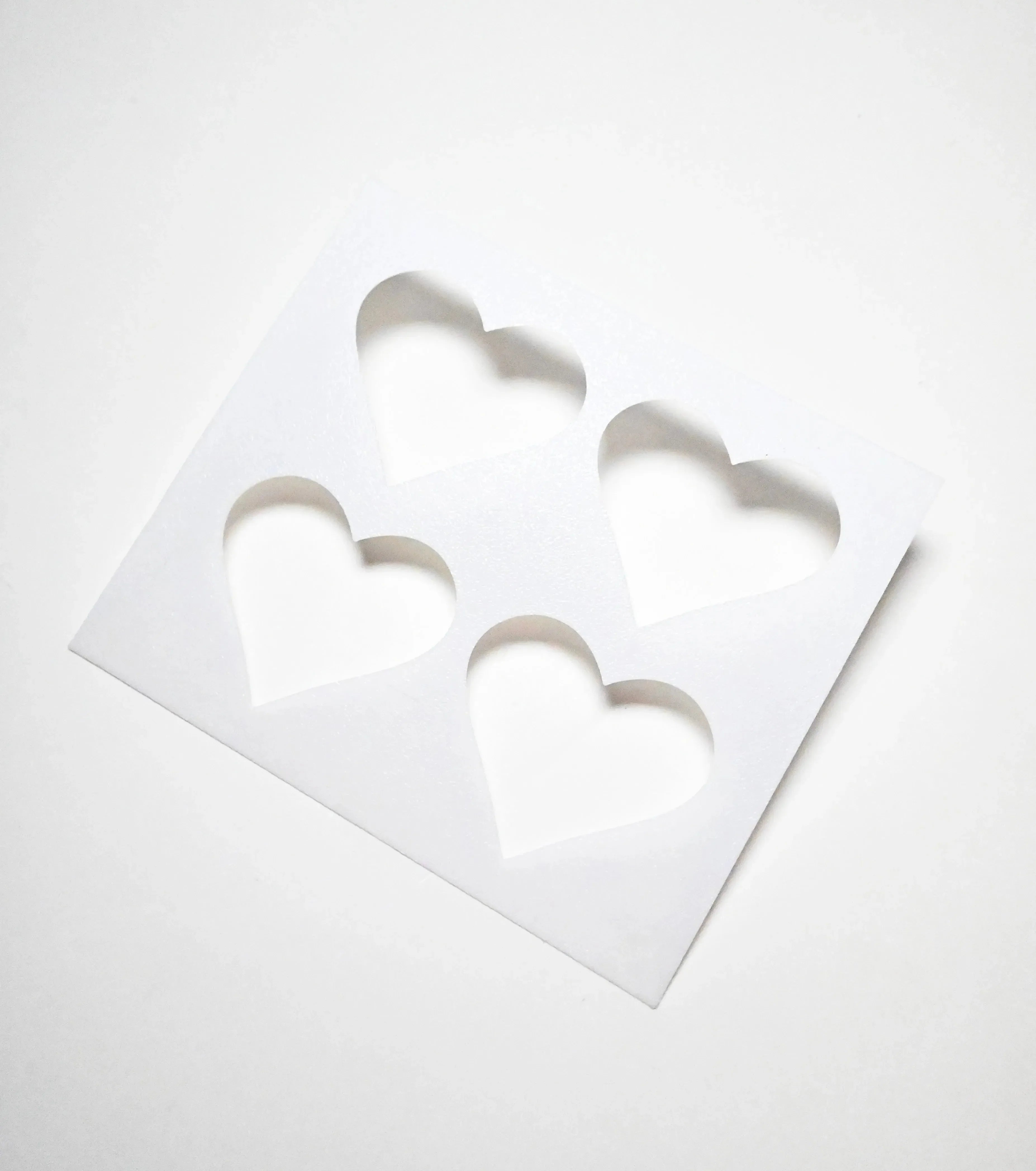White plastic pastry stencil with four symmetrical heart-shaped cutouts.