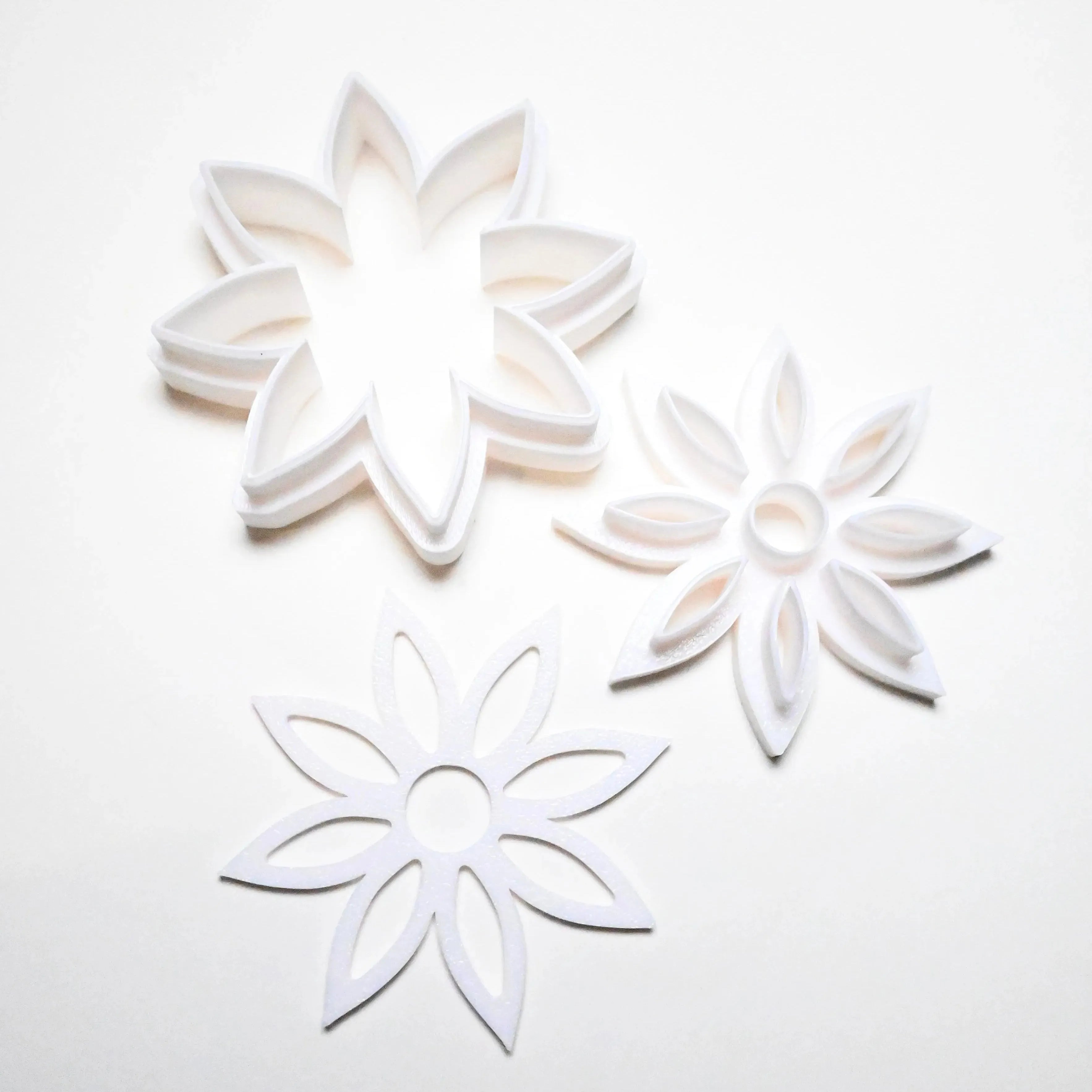 Three white plastic star anise flower cookie cutters in different detailed shapes.