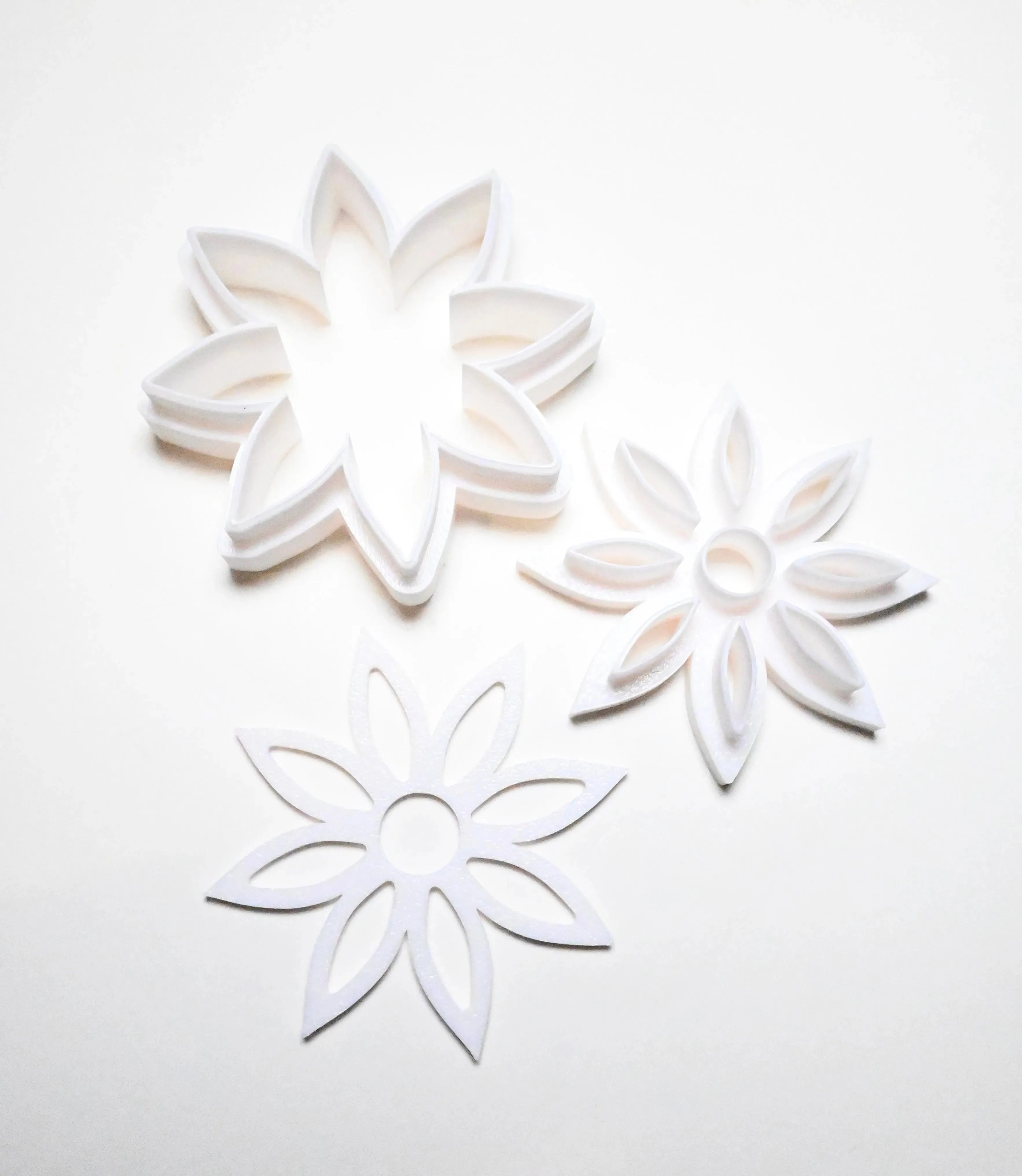 Three white plastic star anise flower cookie cutters in different detailed shapes.