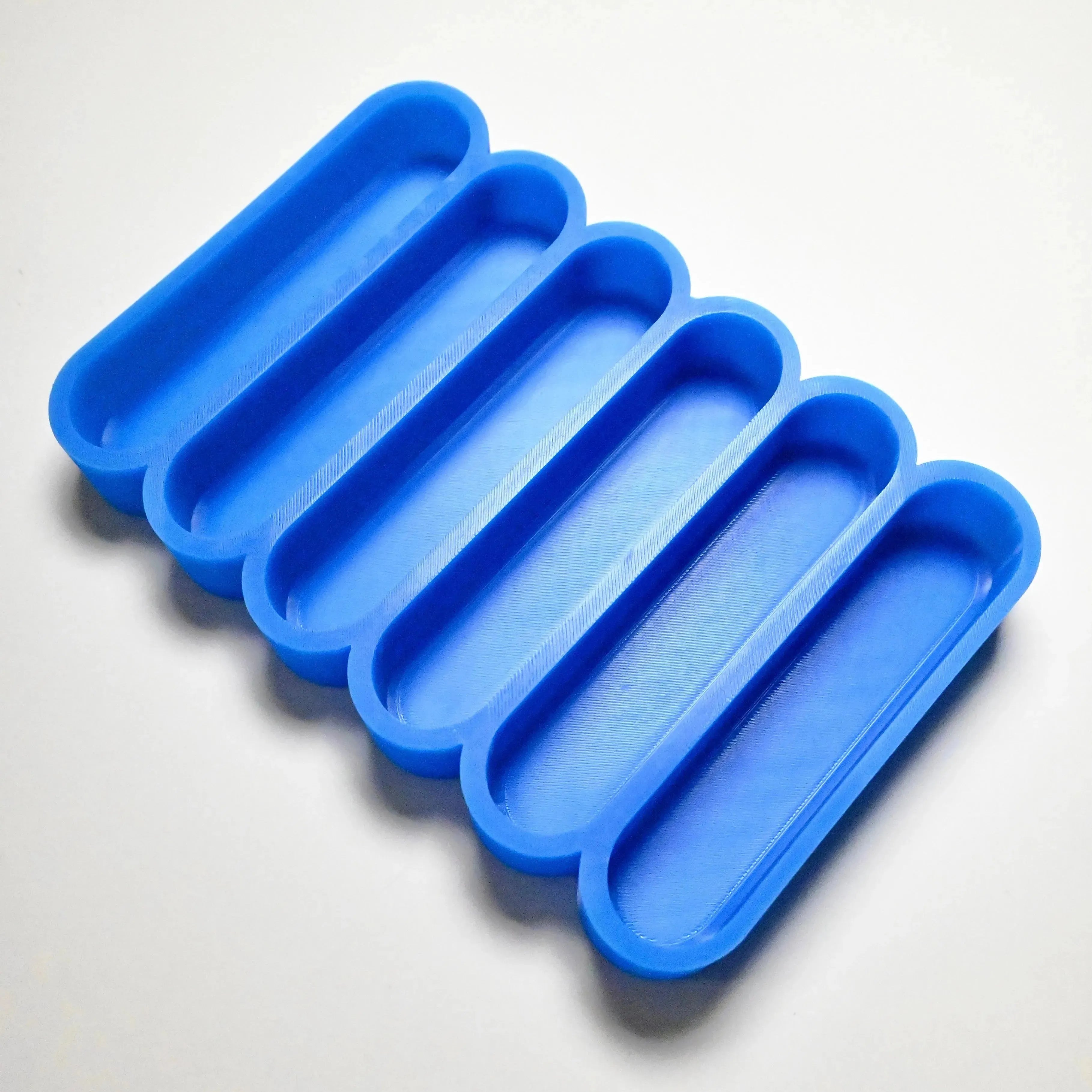 Blue silicone mold with six long, rounded finger-shaped cavities for pastry making.