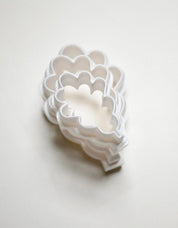 Stacked white plastic oak leaf cookie cutters in graduated sizes.