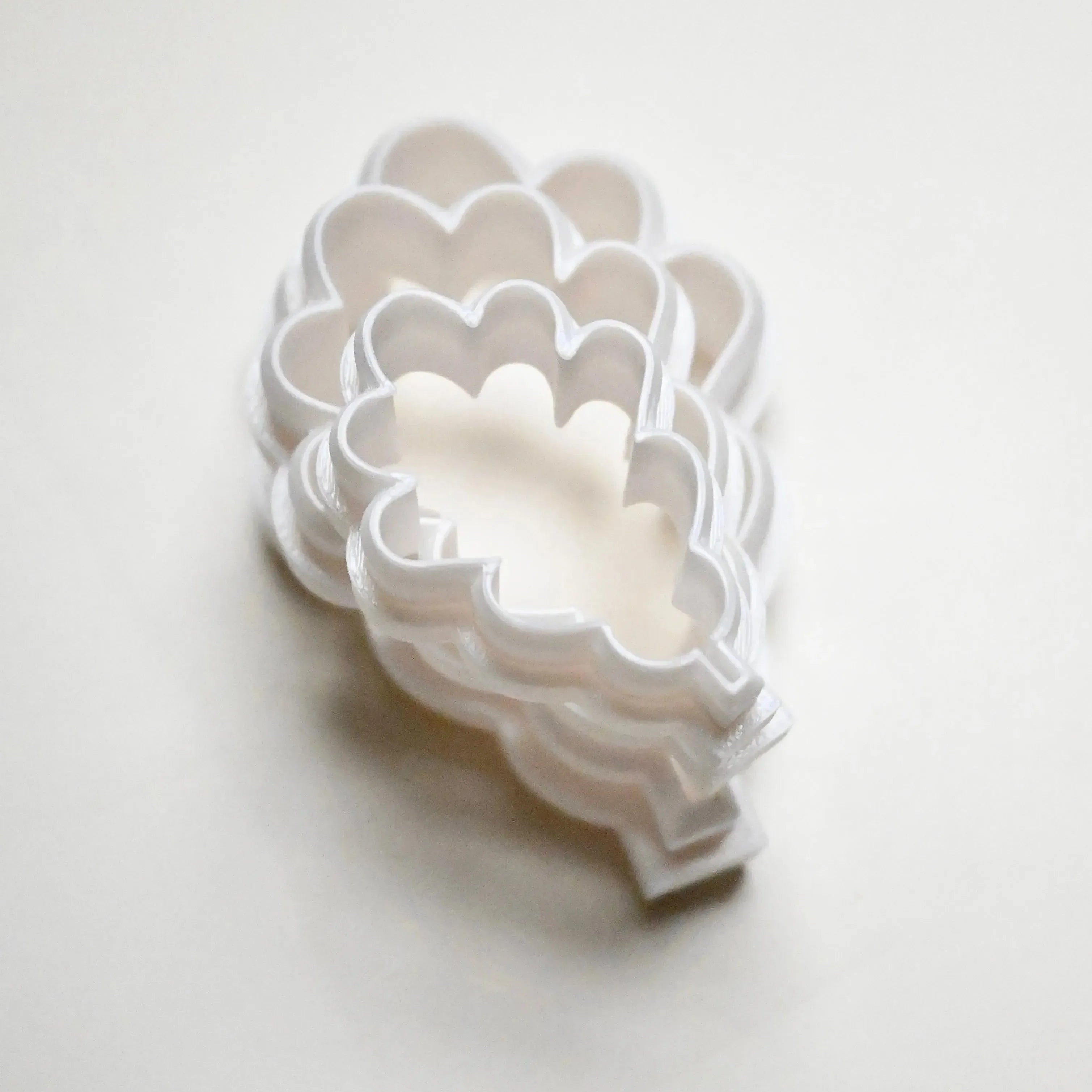 Stacked white plastic oak leaf cookie cutters in graduated sizes.