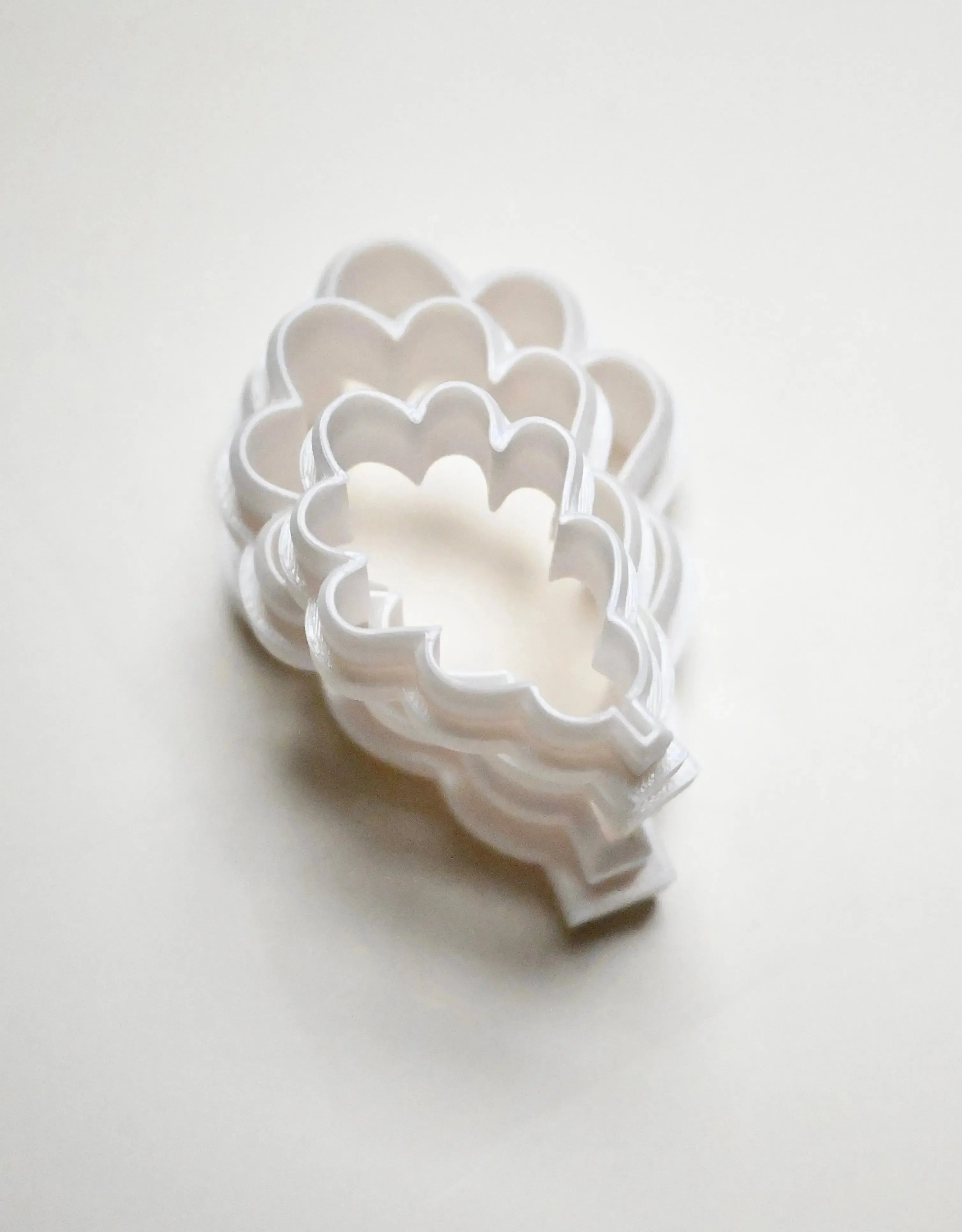 Stacked white plastic oak leaf cookie cutters in graduated sizes.