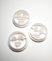Three white plastic round cookie cutters with different smiley face designs.