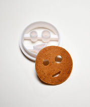 White plastic smiley face cookie cutter next to a round, baked smiley face cookie.