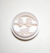 White plastic circular cookie cutter with a smiley face mold featuring round eyes and a curved mouth.