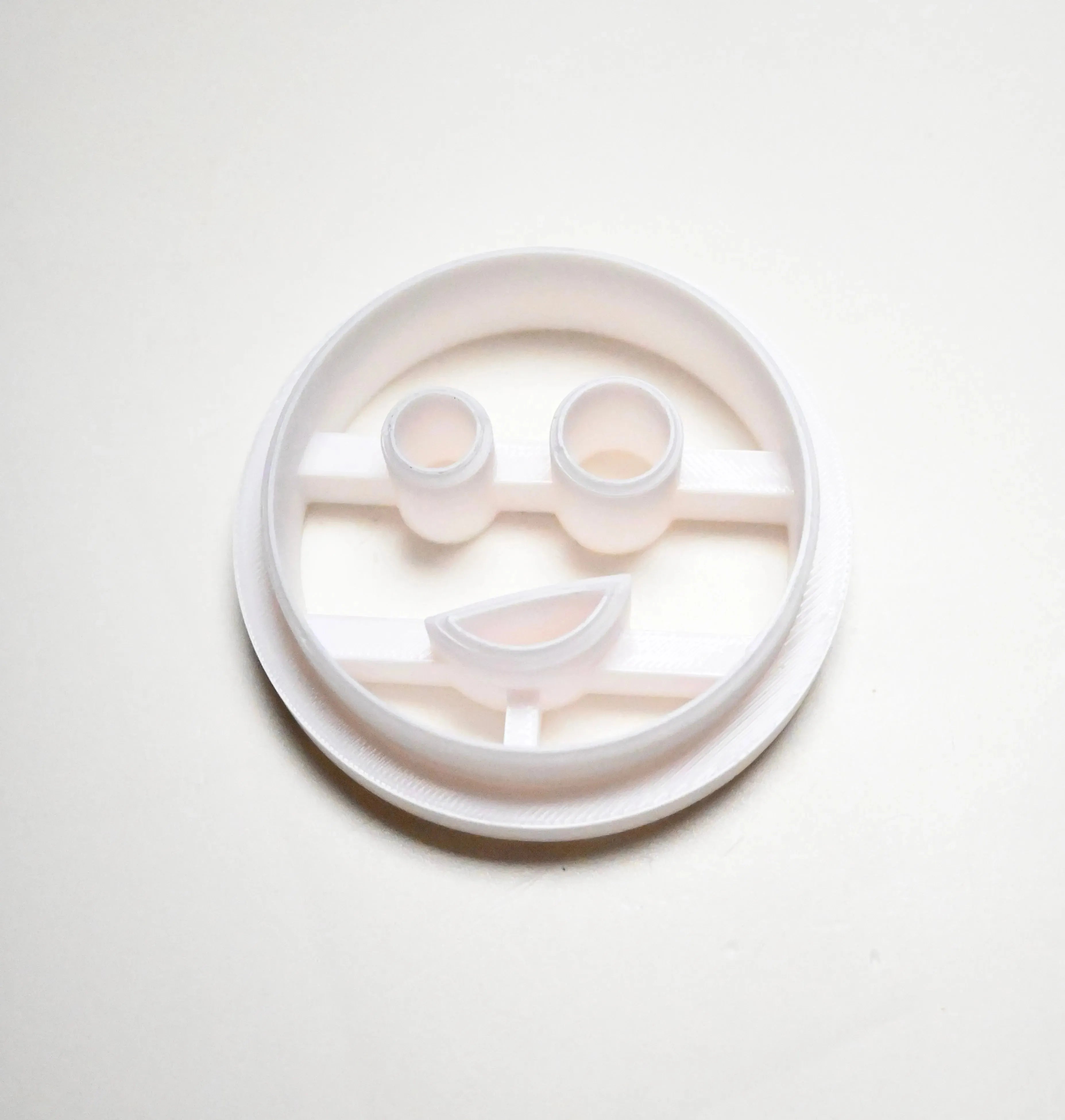 White plastic circular cookie cutter with a smiley face mold featuring round eyes and a curved mouth.