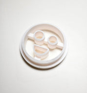 White plastic circular cookie cutter with round eyes and a smiling mouth mold.