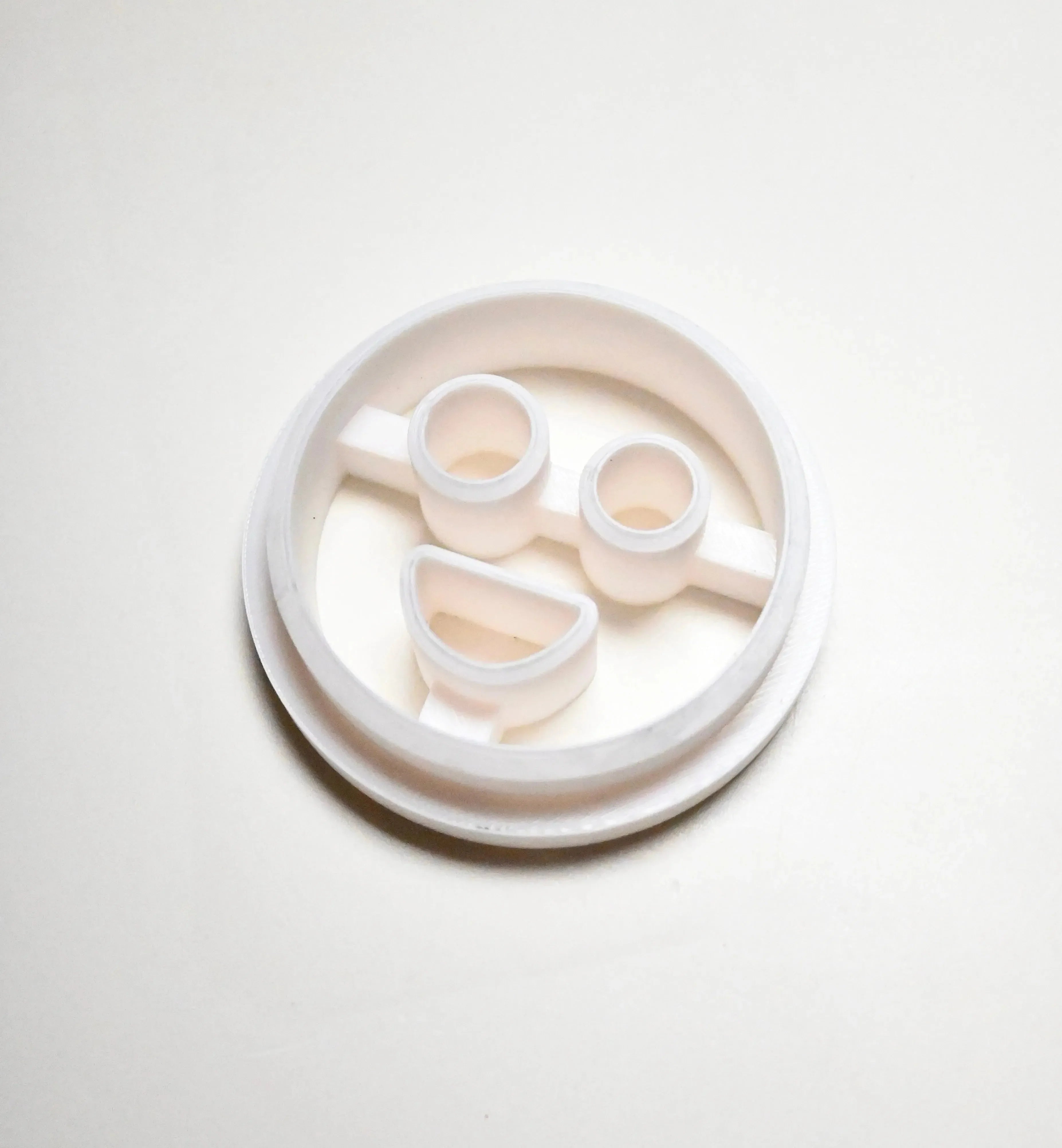 White plastic circular cookie cutter with round eyes and a smiling mouth mold.