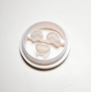 White plastic round cookie cutter with curved eyes and a smiling mouth shape.