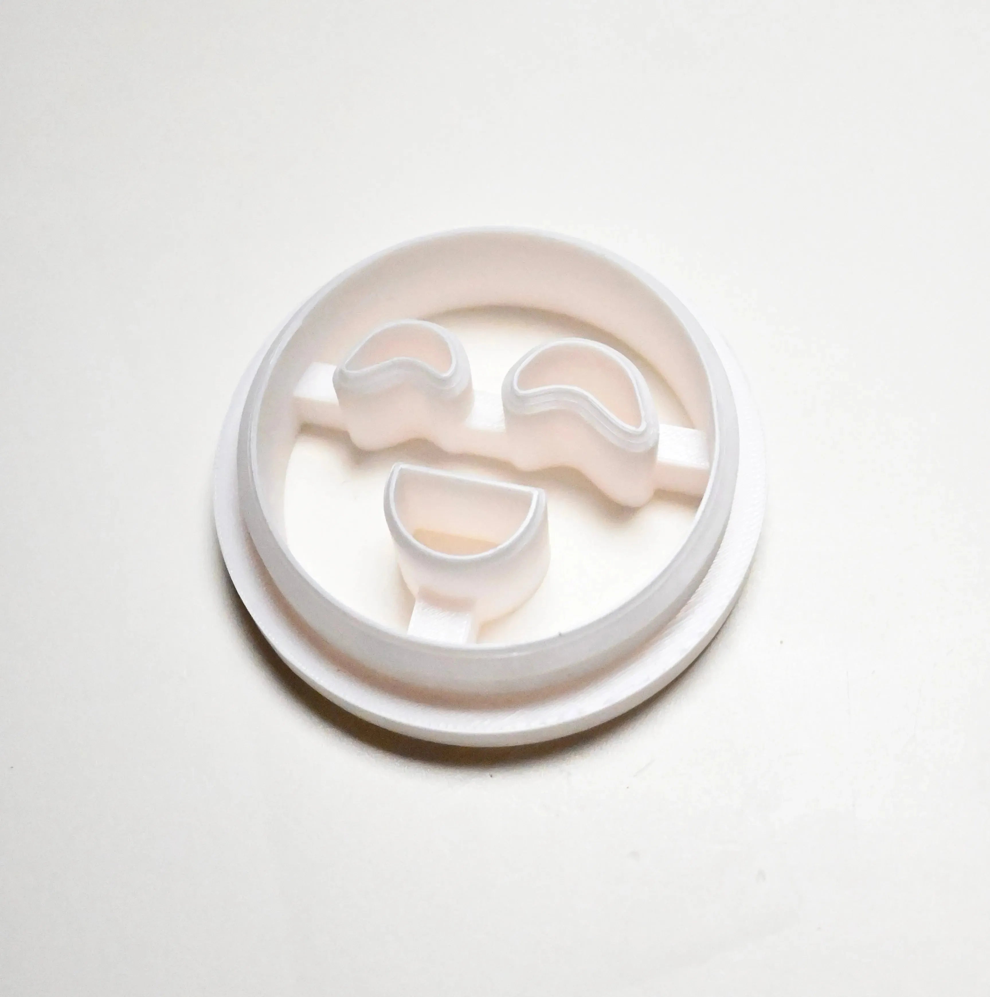 White plastic round cookie cutter with curved eyes and a smiling mouth shape.