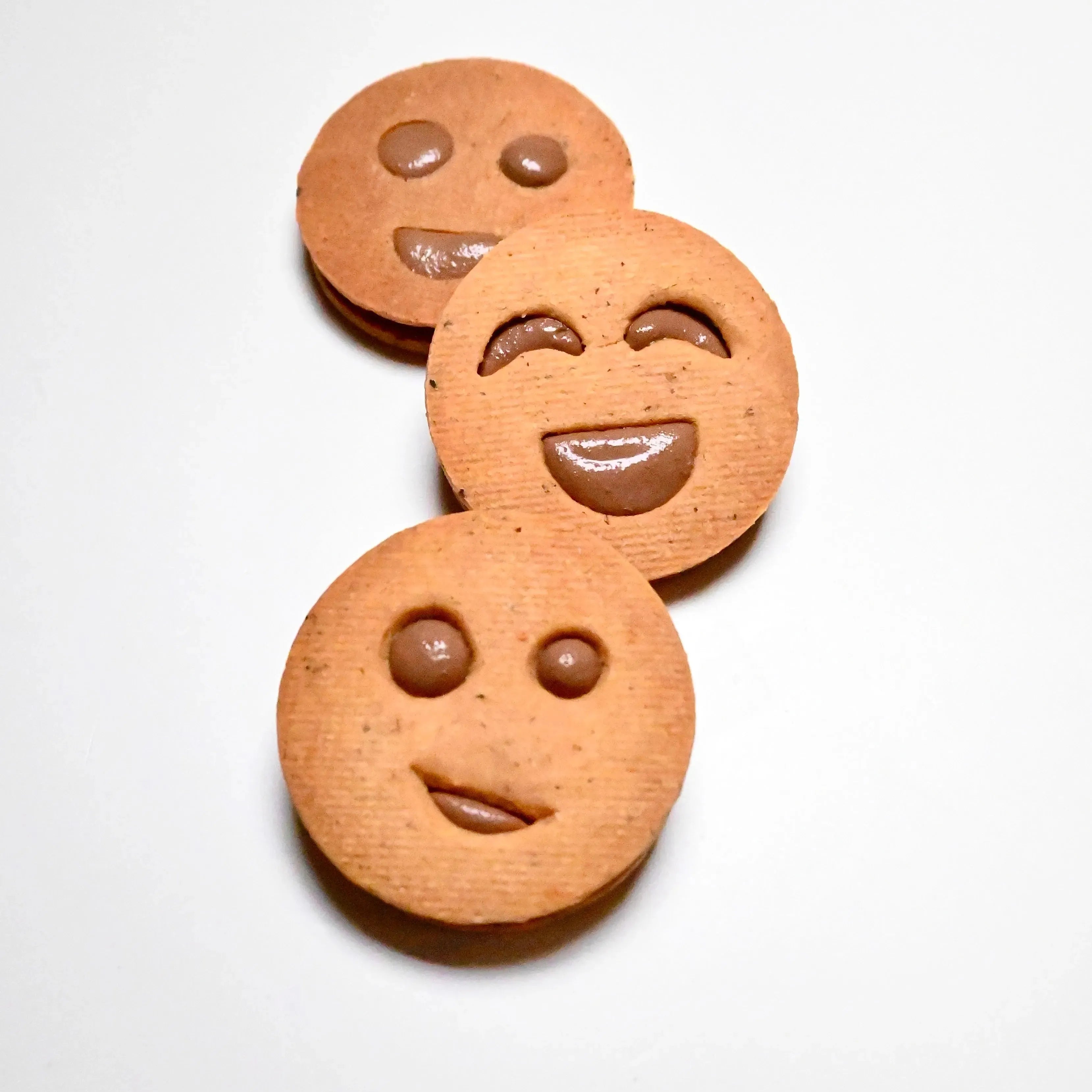 Three round smiley face cookies with chocolate filling, showing different happy expressions.