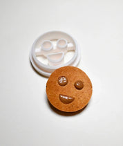 White plastic round smiley face cookie cutter next to a baked cookie with a matching happy face design.