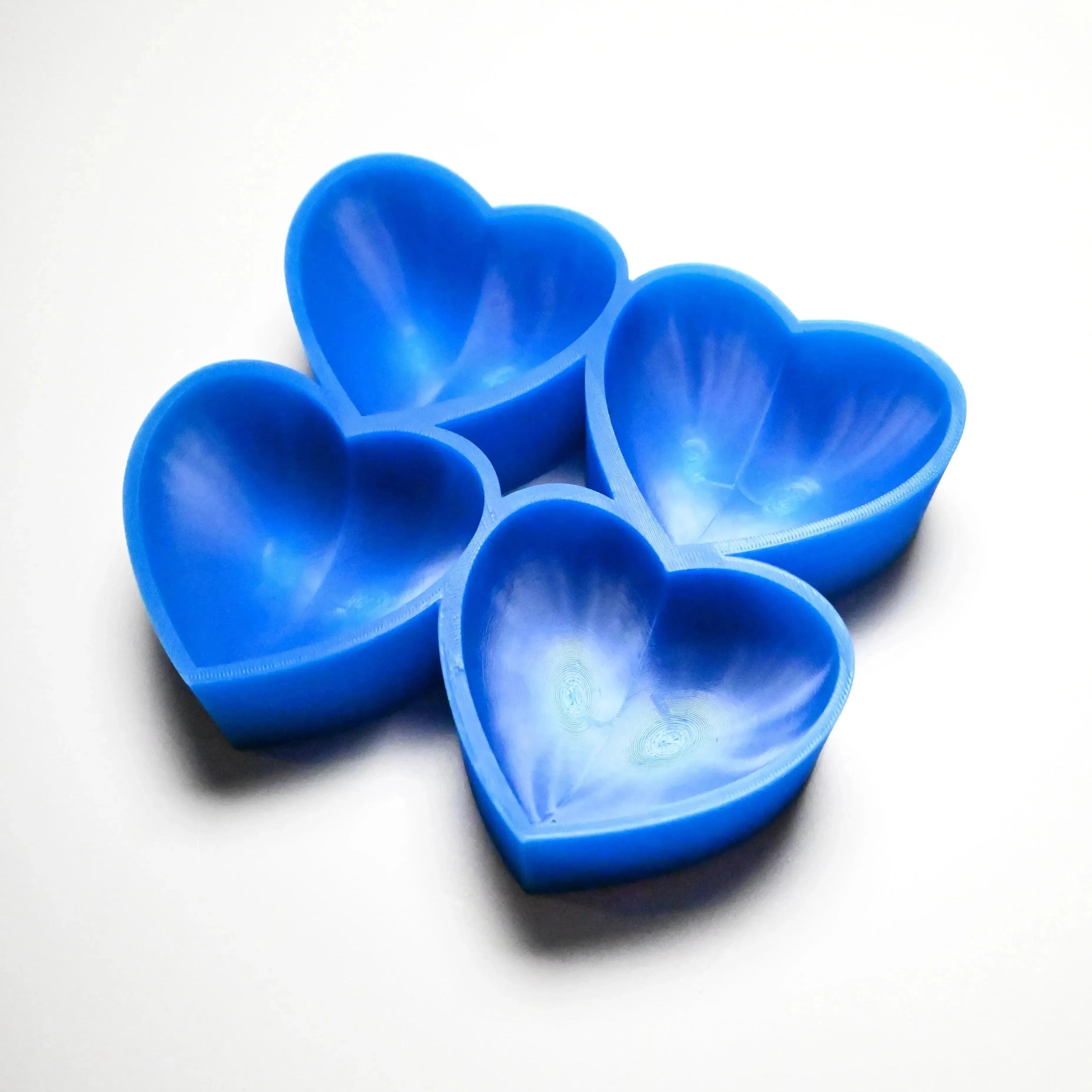 Four blue heart-shaped silicone pastry molds arranged on a white surface.