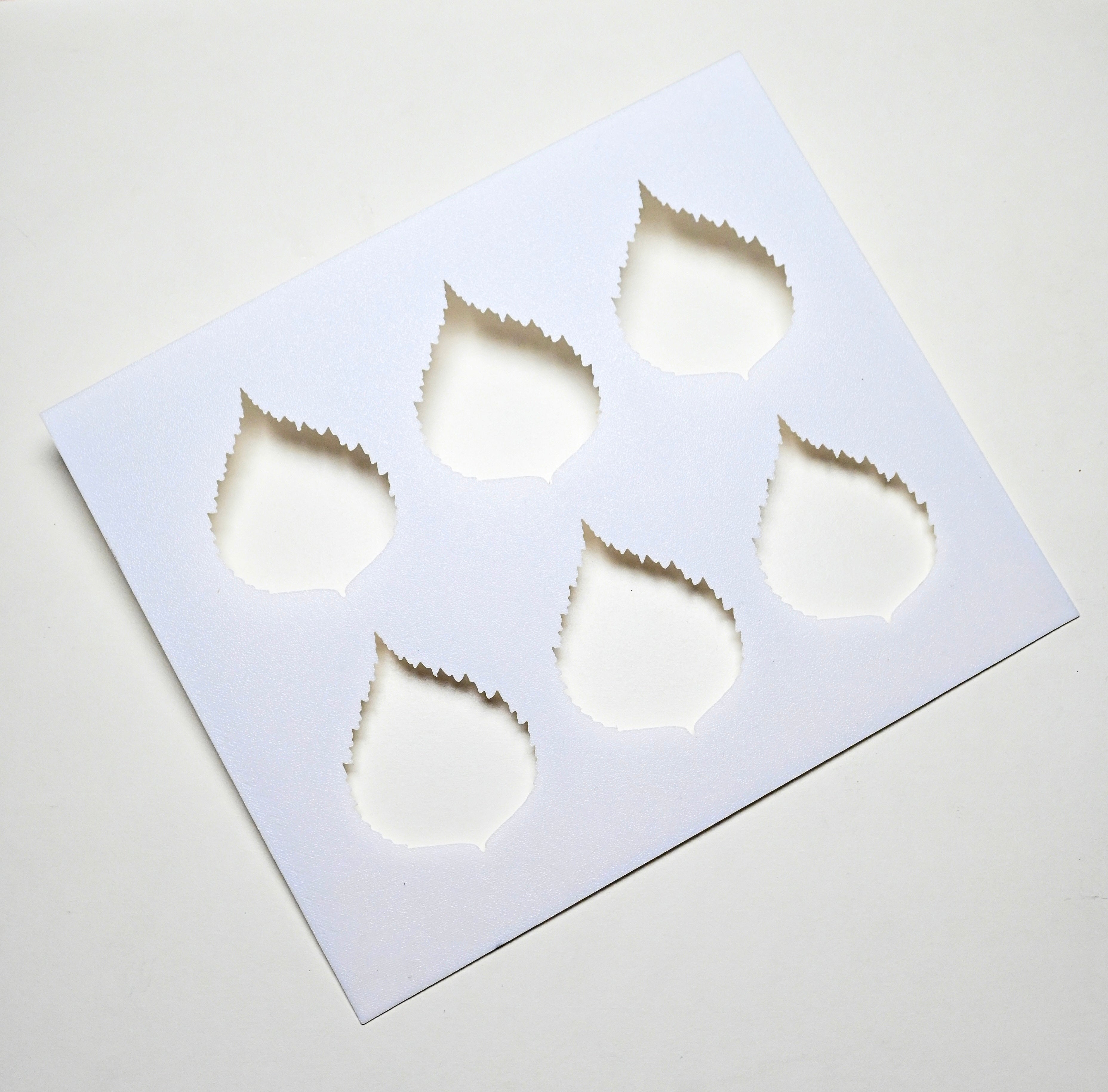 White plastic birch leaf stencil with six serrated leaf-shaped cutouts for pastry decoration.