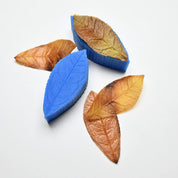 Blue silicone tea leaf molds with realistic brown and yellow pastry leaves showing detailed vein structures.