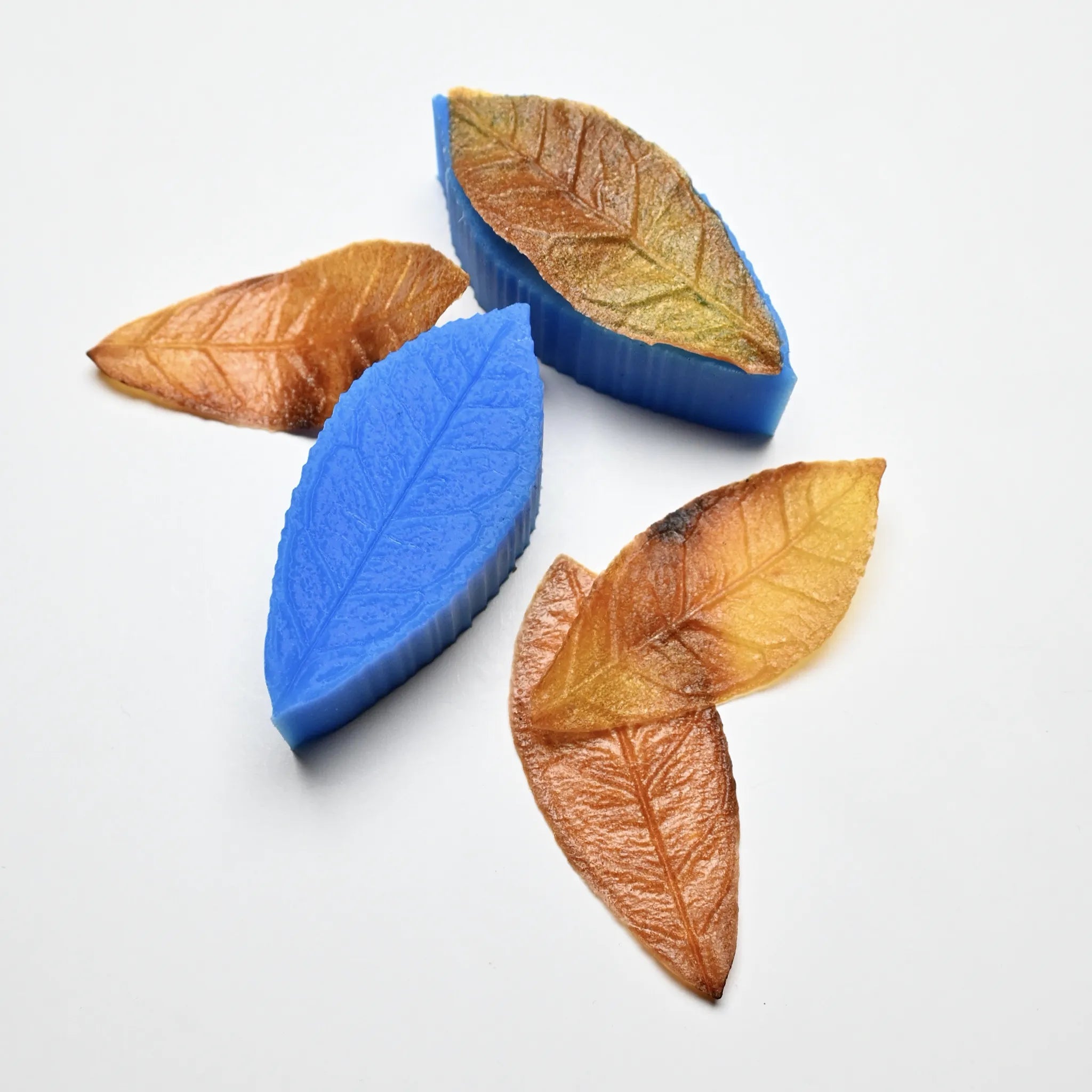 Blue silicone tea leaf molds with realistic brown and yellow pastry leaves showing detailed vein structures.