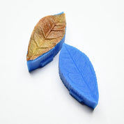 Blue silicone tea leaf press molds showing detailed leaf vein textures and a brown pastry leaf.
