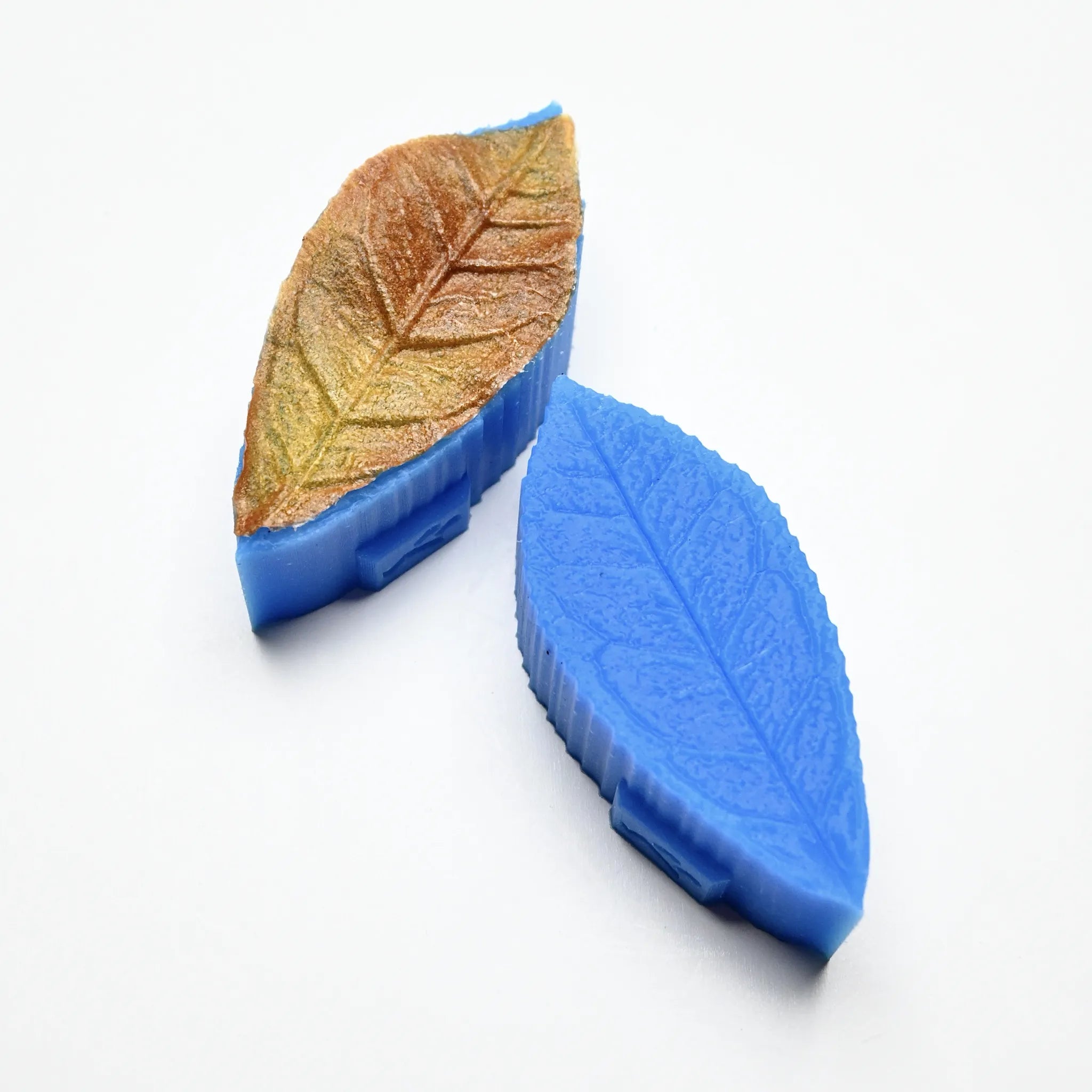 Blue silicone tea leaf press molds showing detailed leaf vein textures and a brown pastry leaf.