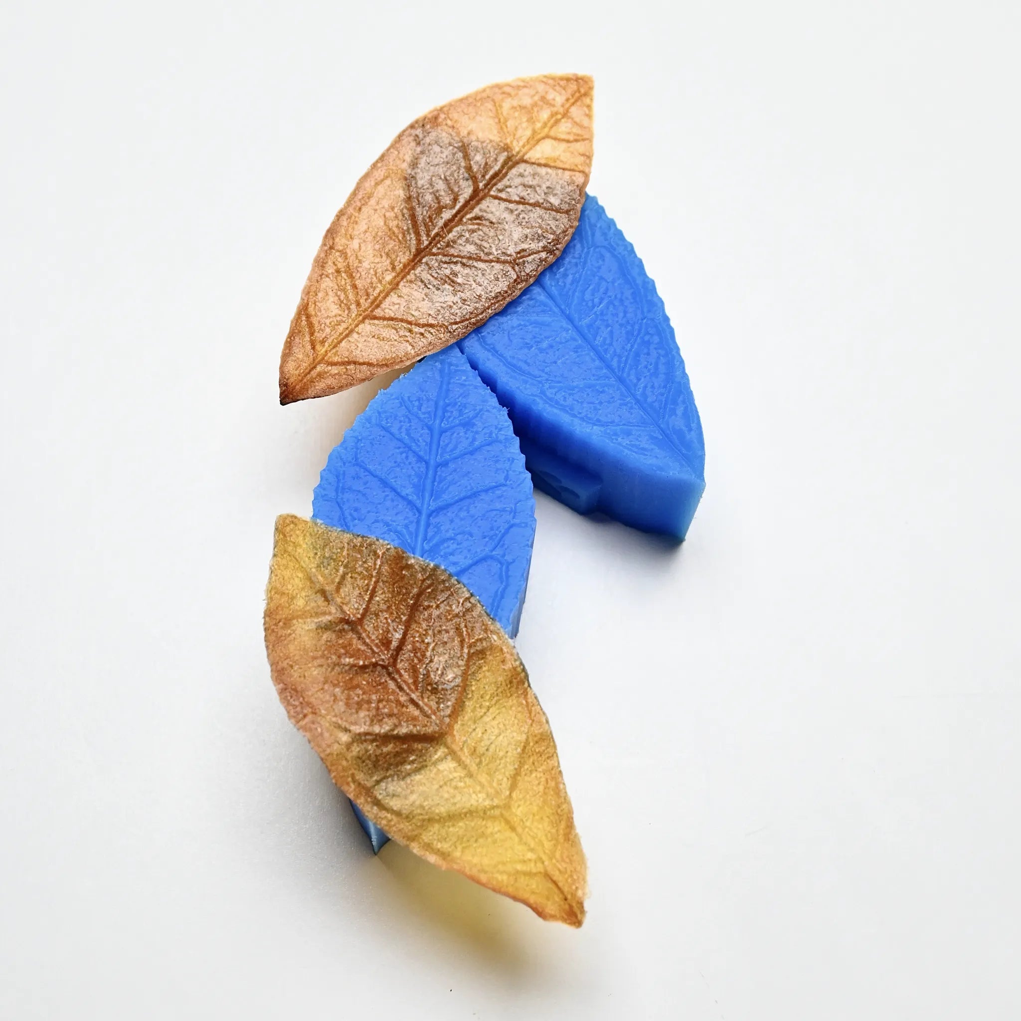 Blue silicone tea leaf molds shown with realistic brown pastry leaves highlighting detailed vein textures.