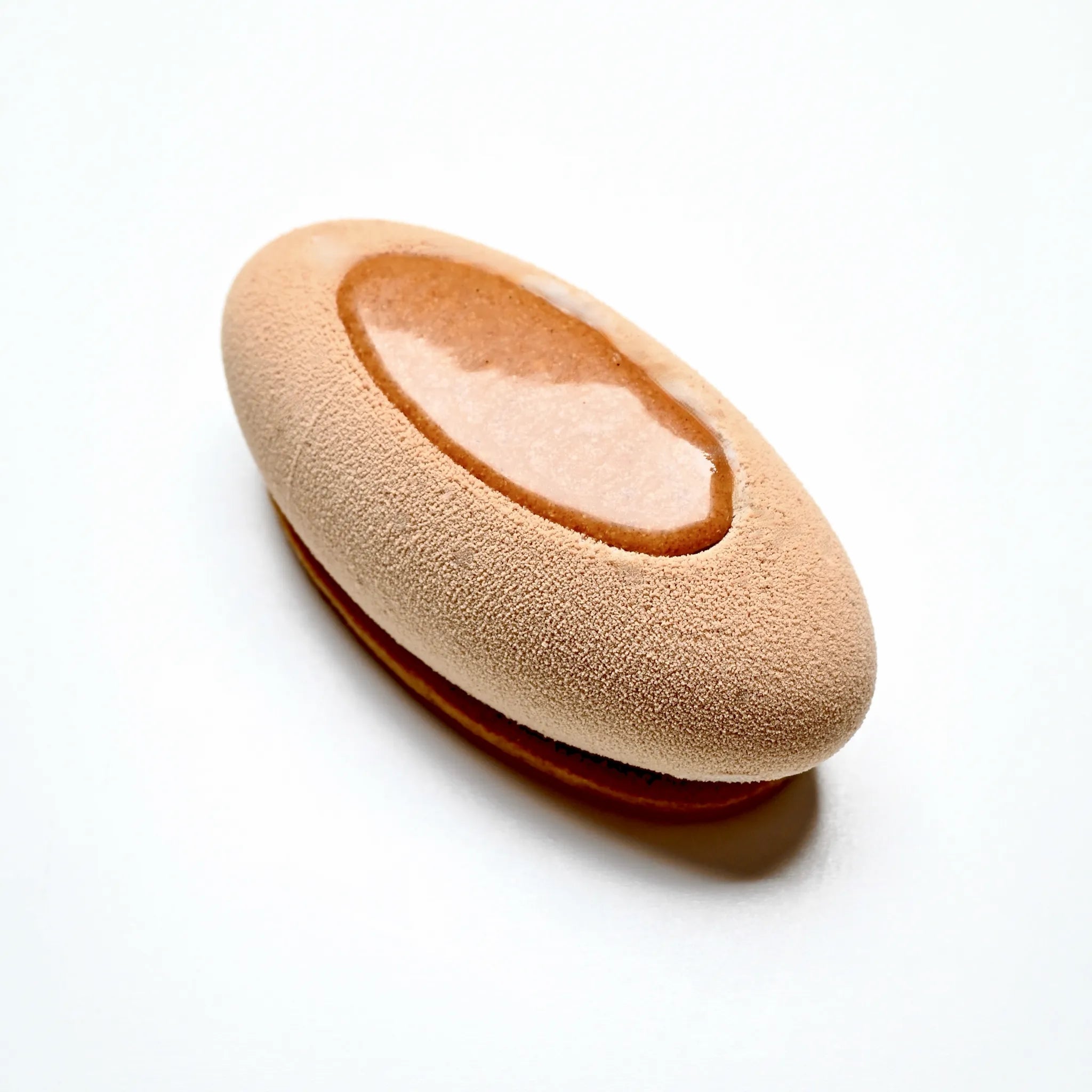 Elliptical beige mousse dessert with a smooth glaze insert on a white background.