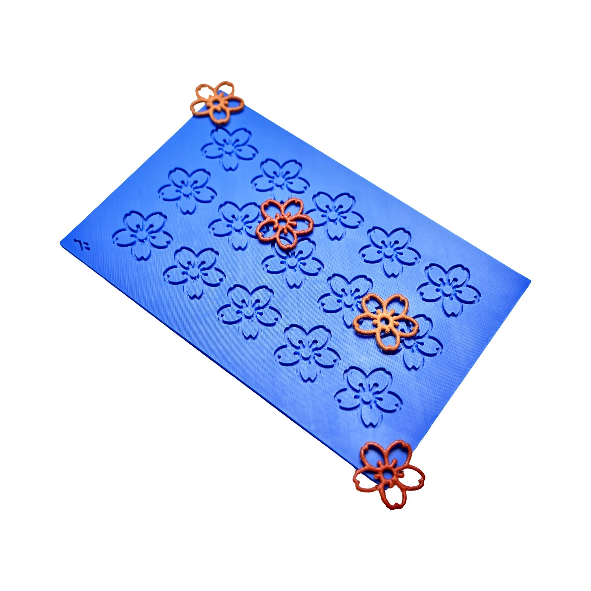 Blue silicone mat with cherry blossom shaped molds and orange tuile decorations.