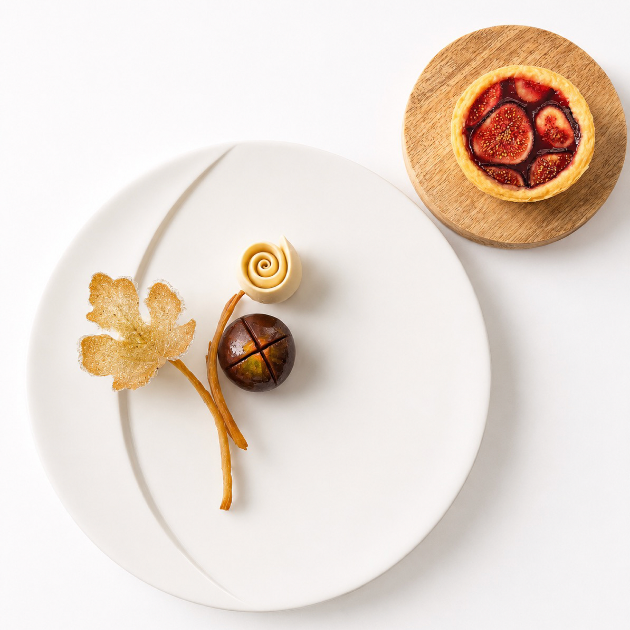 Detailed sugar fig leaf and edible decorations on a white plate next to a small fig tart.