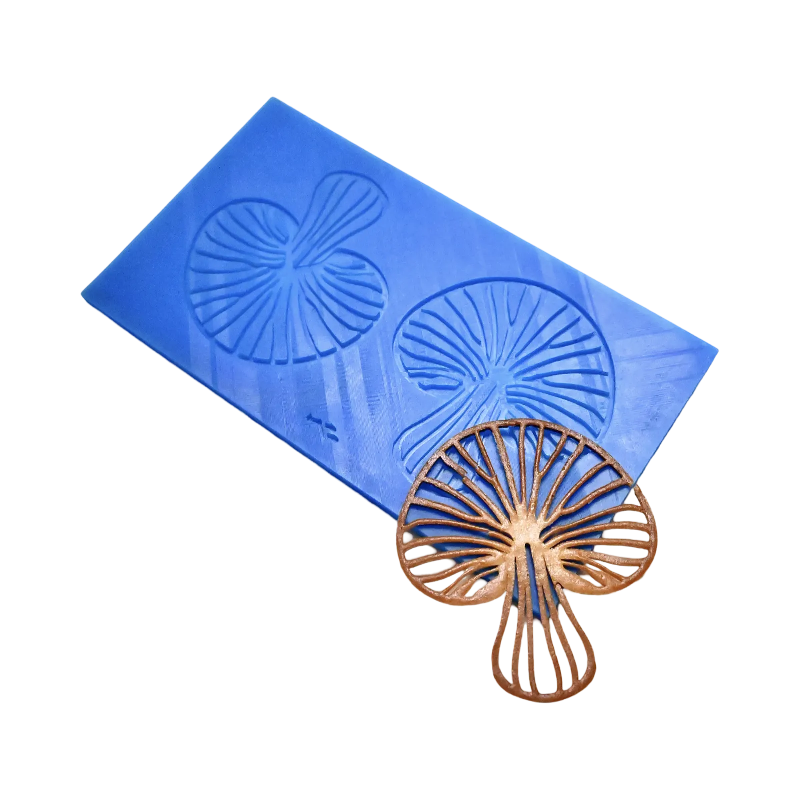 Blue silicone mat with mushroom-shaped tuile molds next to a brown, detailed mushroom garnish.